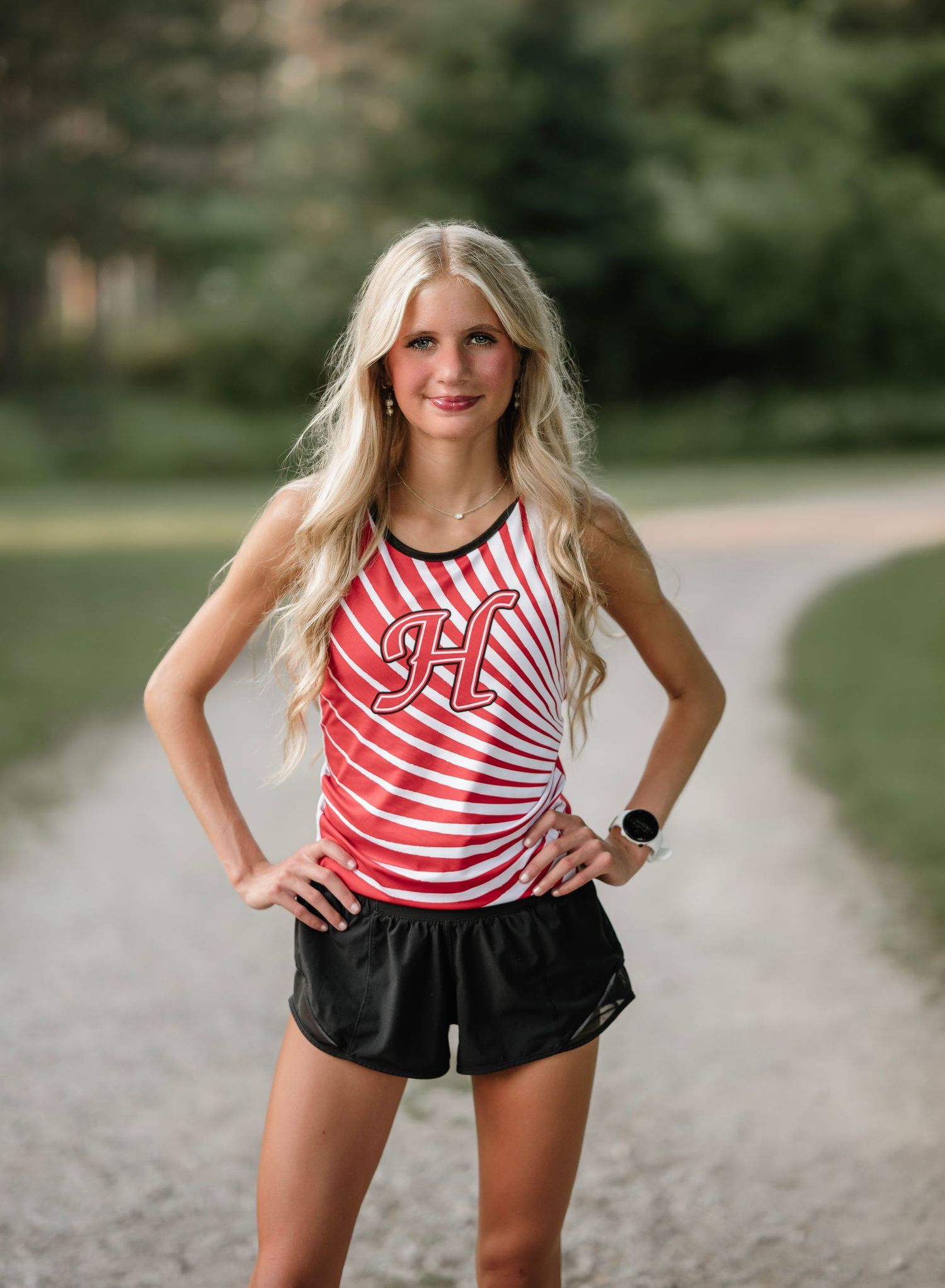 Athletic woman in red and white striped tank top and black shorts posing on gravel path outdoors.