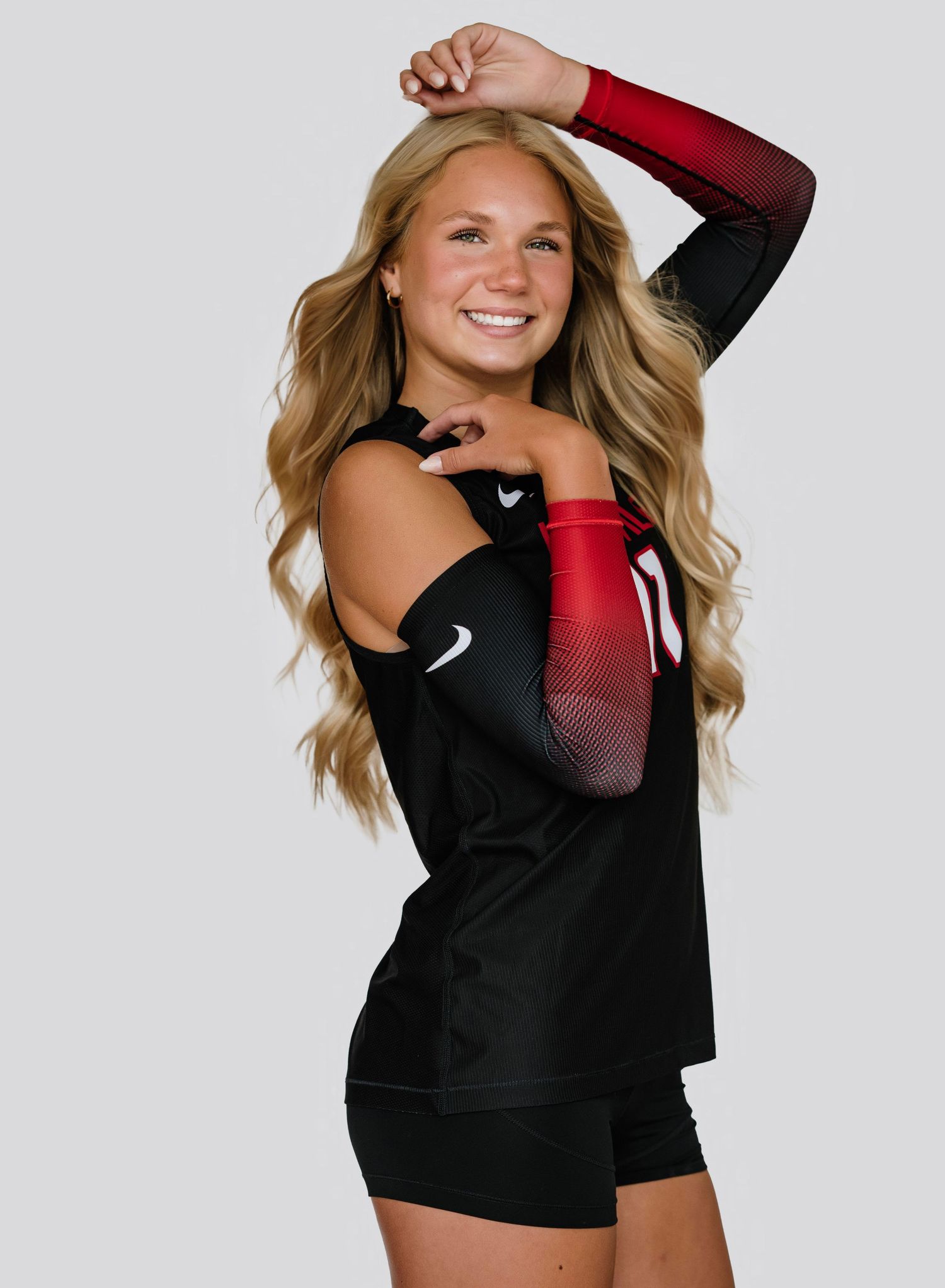 Young female volleyball player in black and red Nike uniform smiling confidently in a professional sports portrait photo.