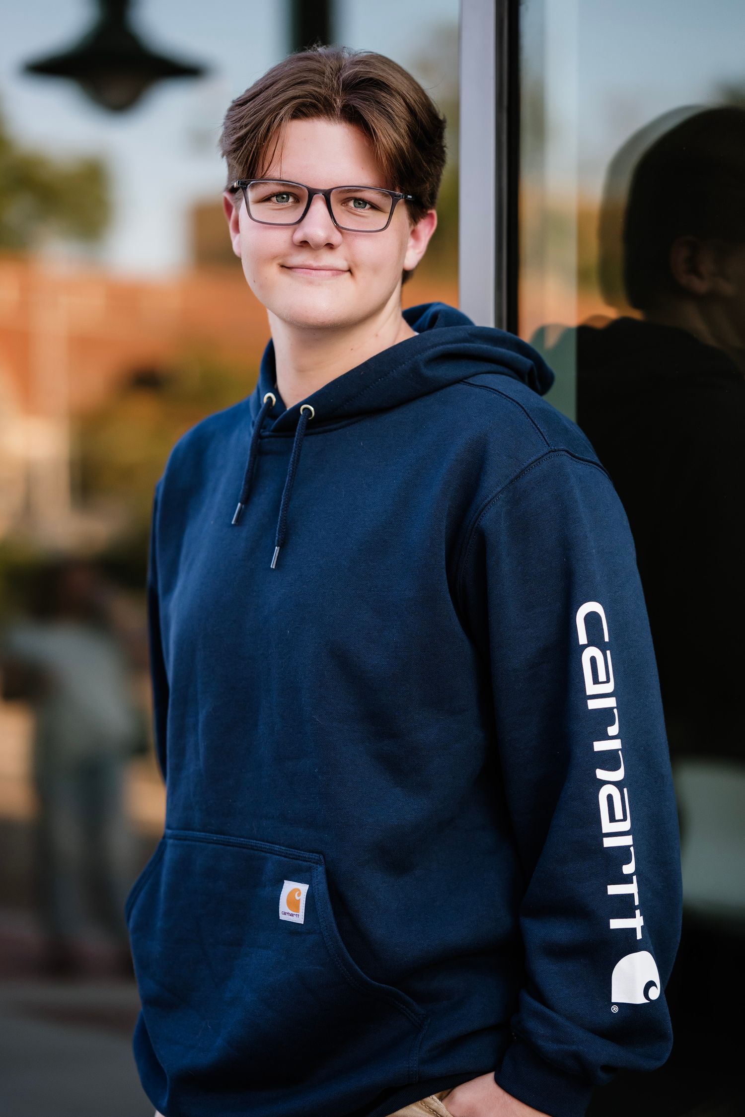 A person wearing glasses and a navy blue Carhartt hoodie poses in different angles outdoors at sunset.