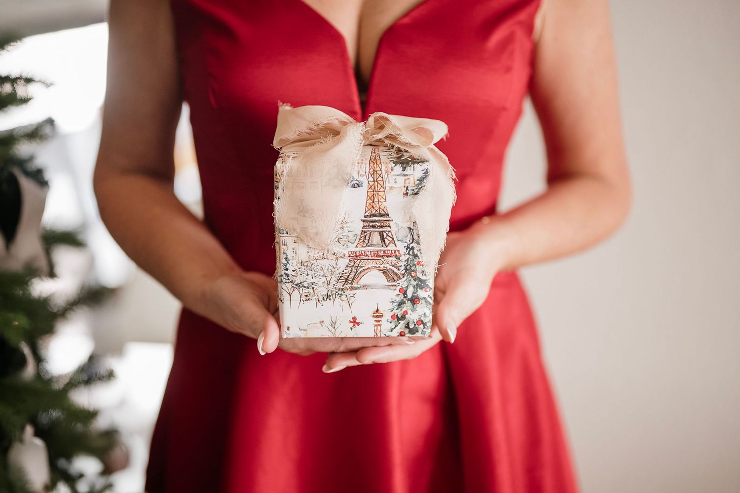 A person in a red dress holds a decorative gift box with an Eiffel Tower design.