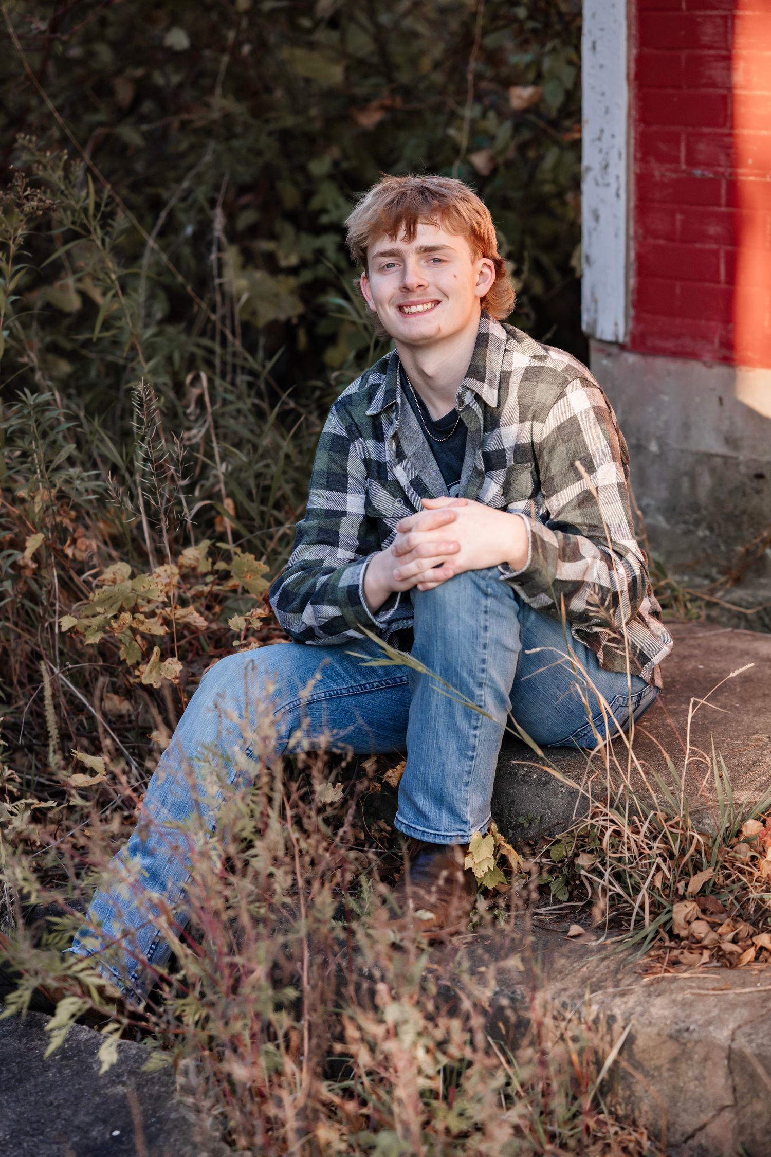 A series of outdoor portrait photos showing someone sitting on rocks near a red brick wall in casual clothing.