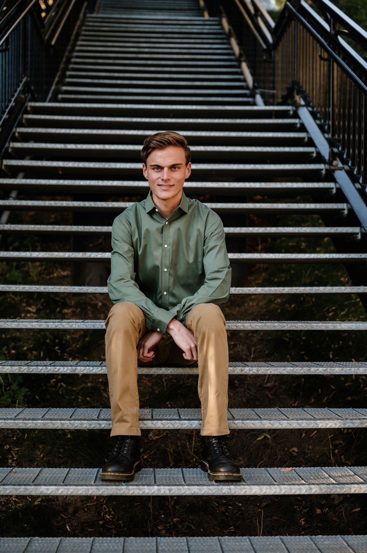 Portrait of senior sitting on concrete steps wearing a green button-down shirt and khaki pants.