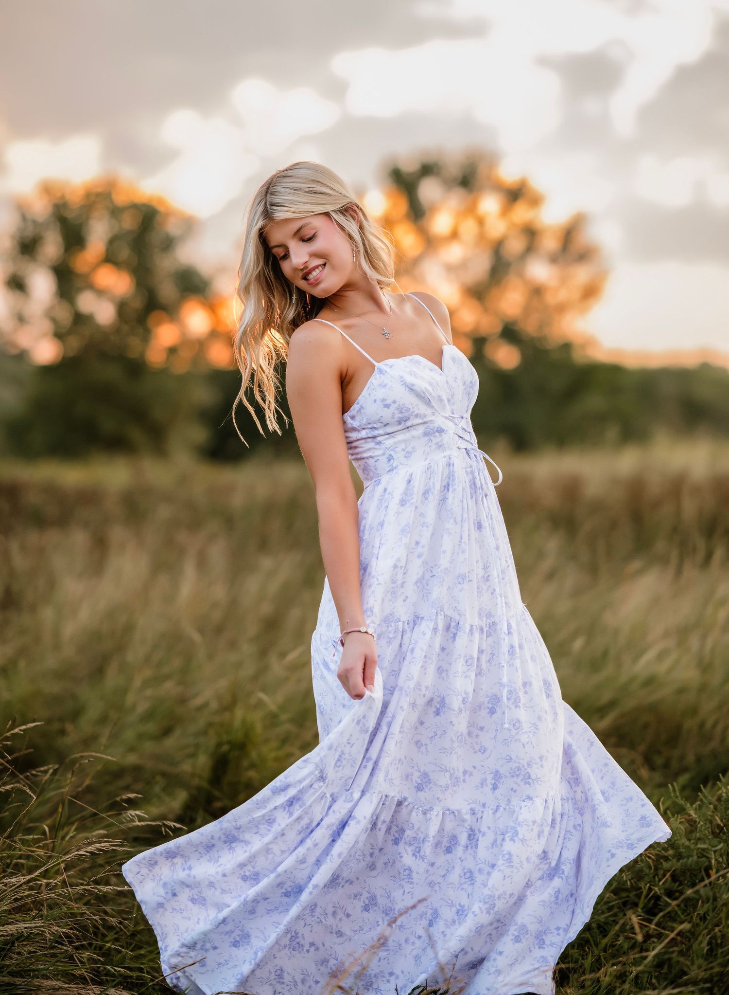 A flowing white floral sundress moves in the breeze during golden hour in a grassy meadow at sunset.