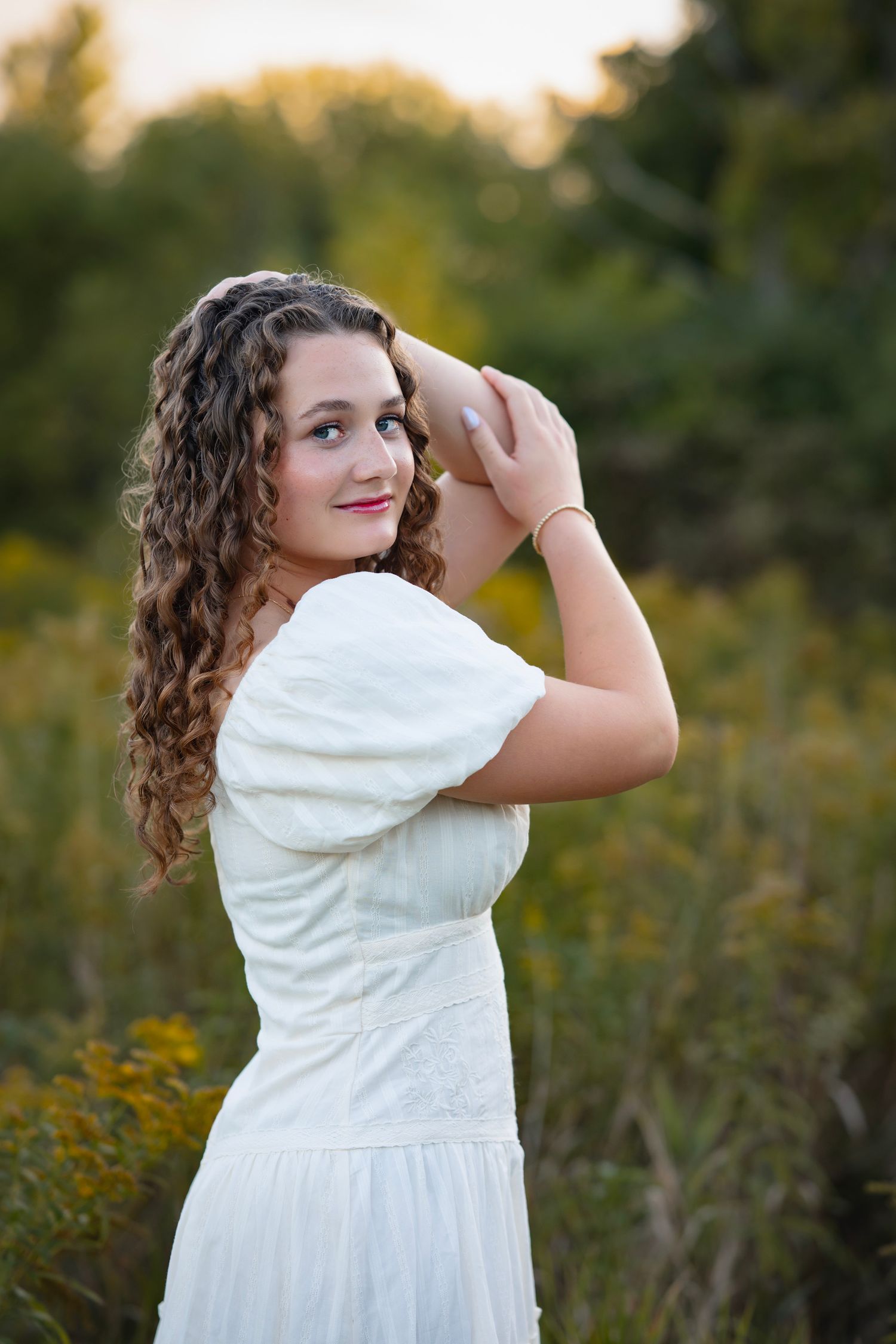 A person in a flowing white dress poses gracefully in a field of wildflowers during golden hour.