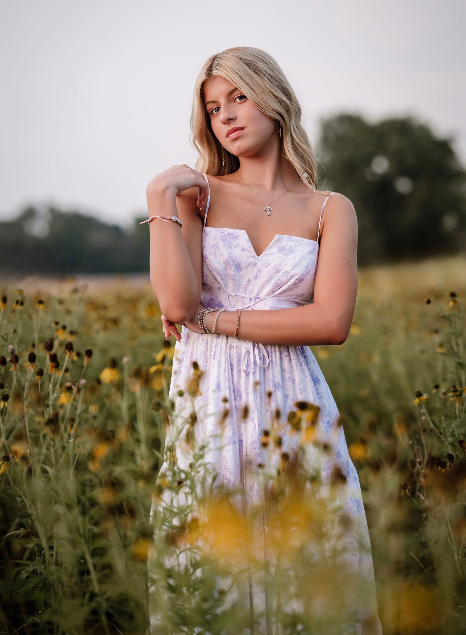 Young blonde woman in floral sundress posing gracefully in a wildflower field at golden hour.