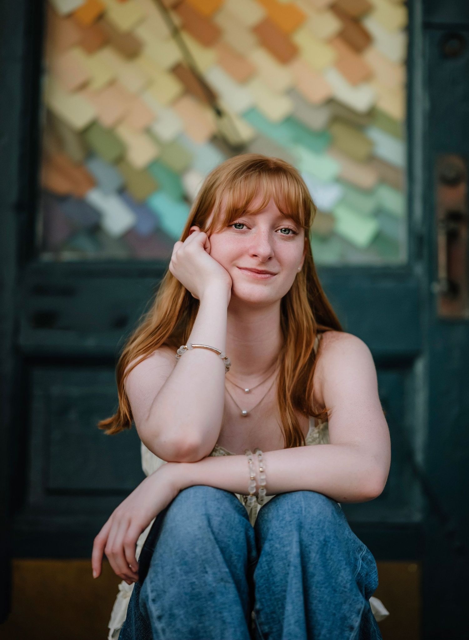 Portrait of someone sitting casually against a dark background with colorful paper decorations on the wall.