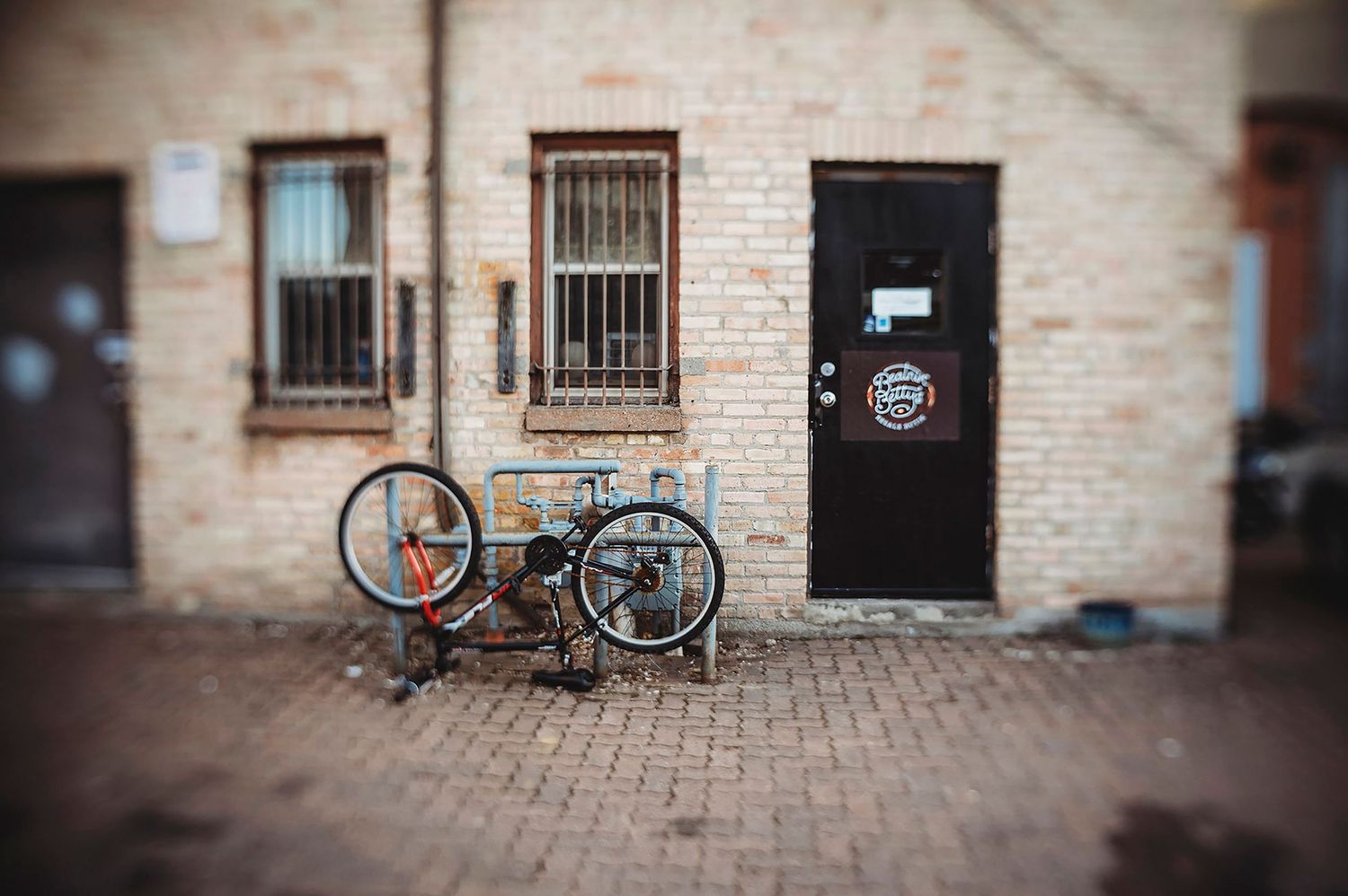 A series of brick buildings with parked bicycles and barred windows along a cobblestone street.