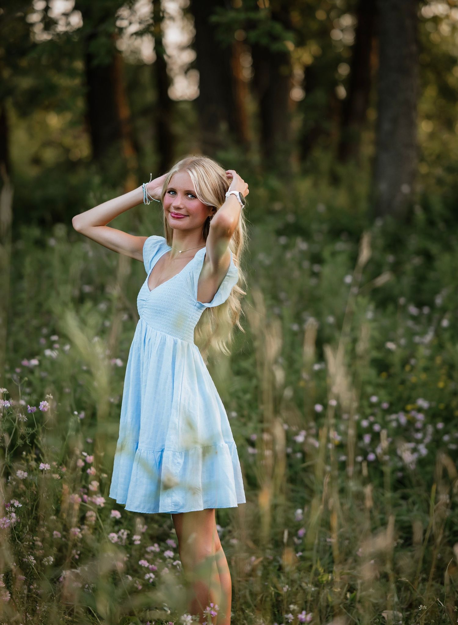 A person in a light blue summer dress twirls playfully in a wildflower meadow at golden hour.