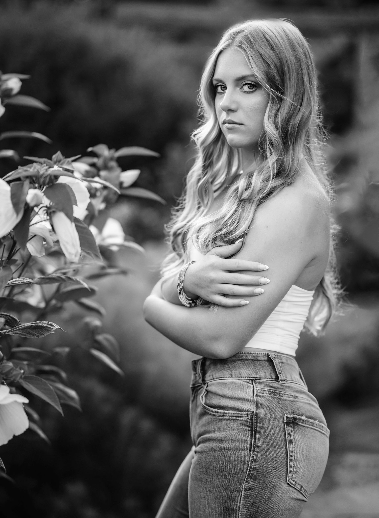 Black and white artistic portrait series showing a woman in denim and white top posing against foliage in natural light.