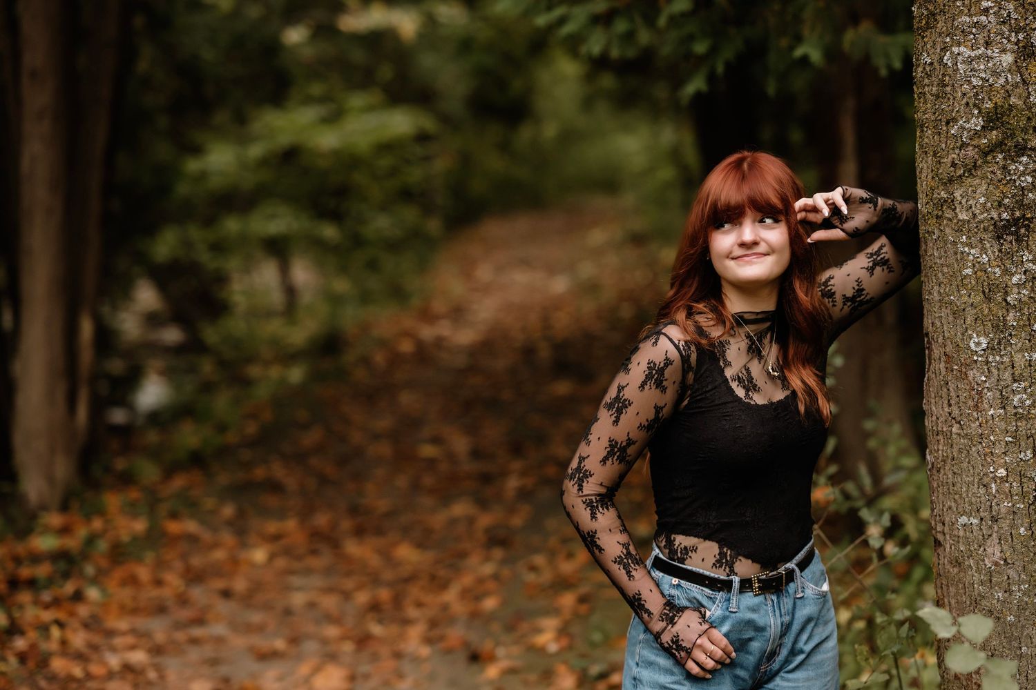 A person in a black sweater walks through an autumn forest path covered in fallen orange leaves.