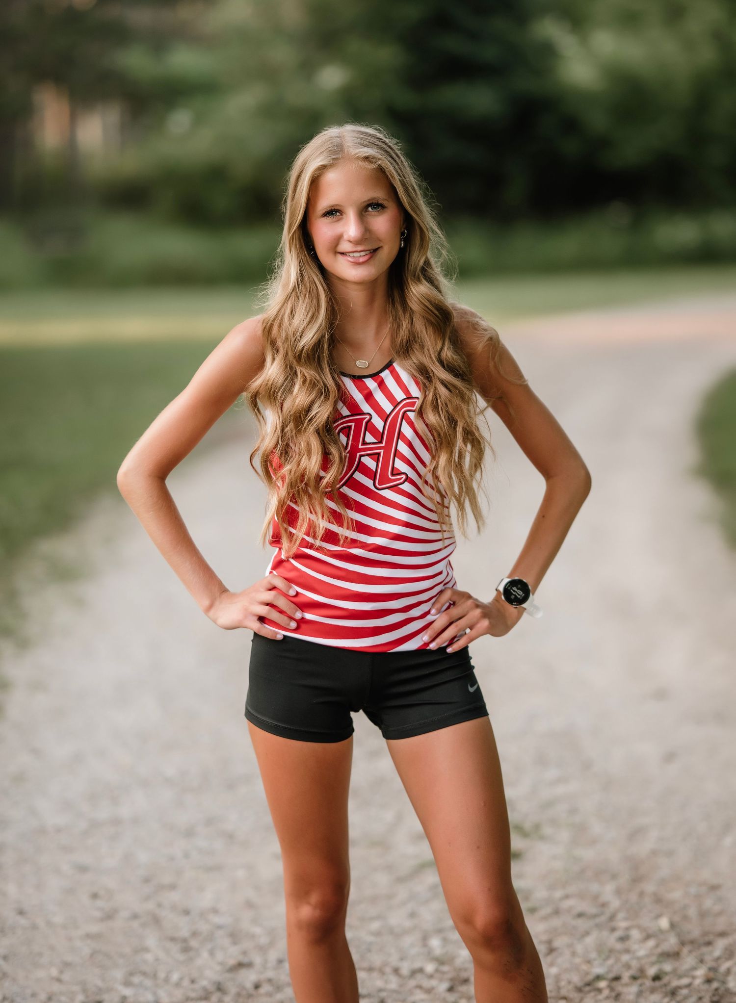 A person wearing a red and white striped tank top and black shorts poses outdoors on a gravel path.