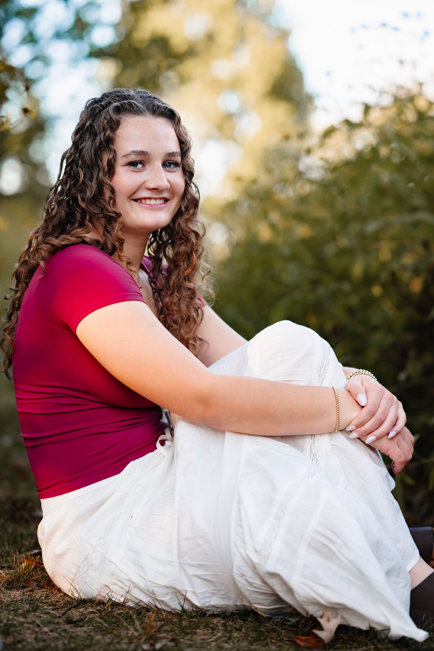 A person in a burgundy top and white skirt poses outdoors in a series of casual portraits with natural lighting.