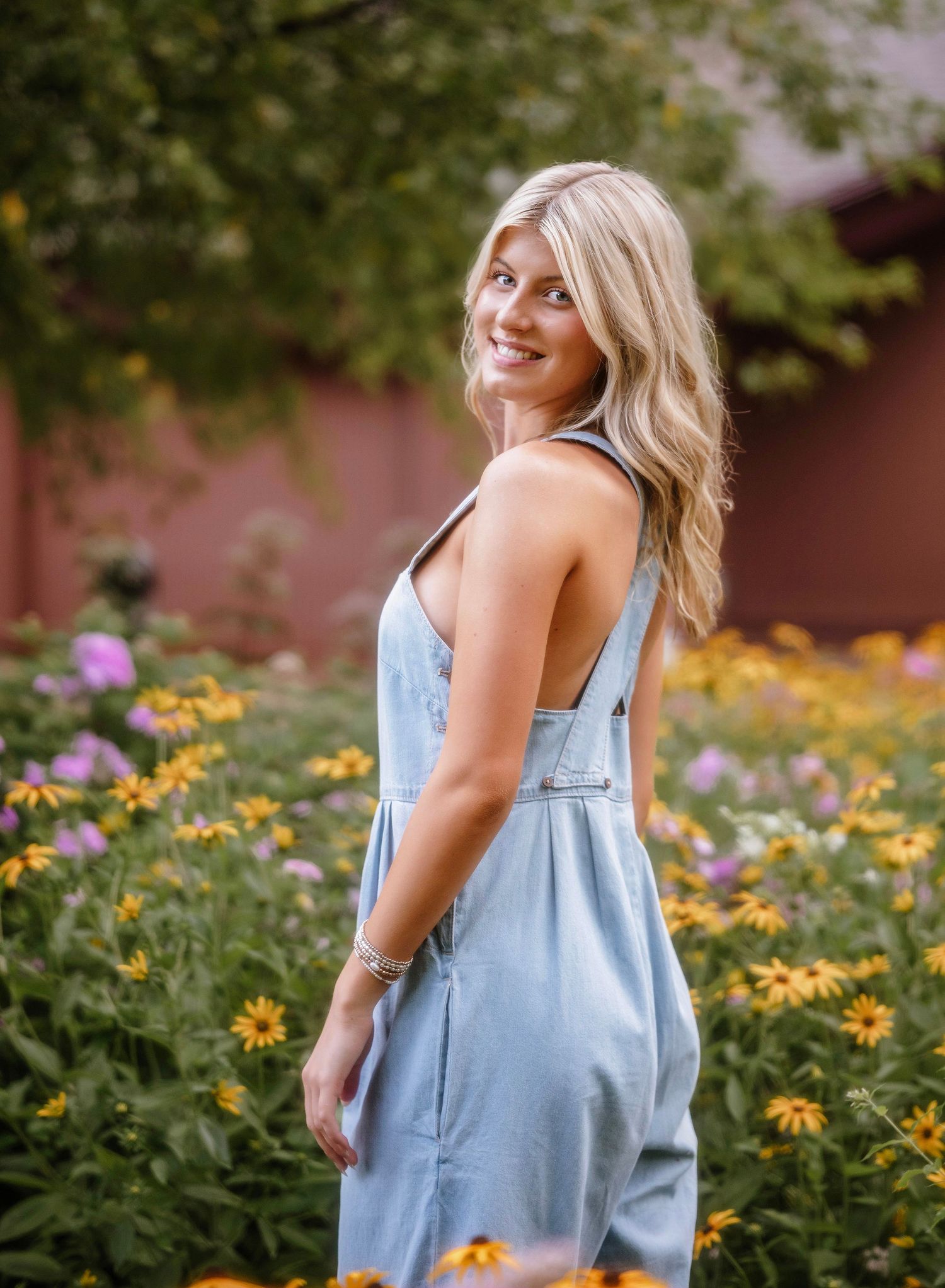 A person in a light blue denim dress twirls playfully in a garden filled with blooming yellow and purple flowers.
