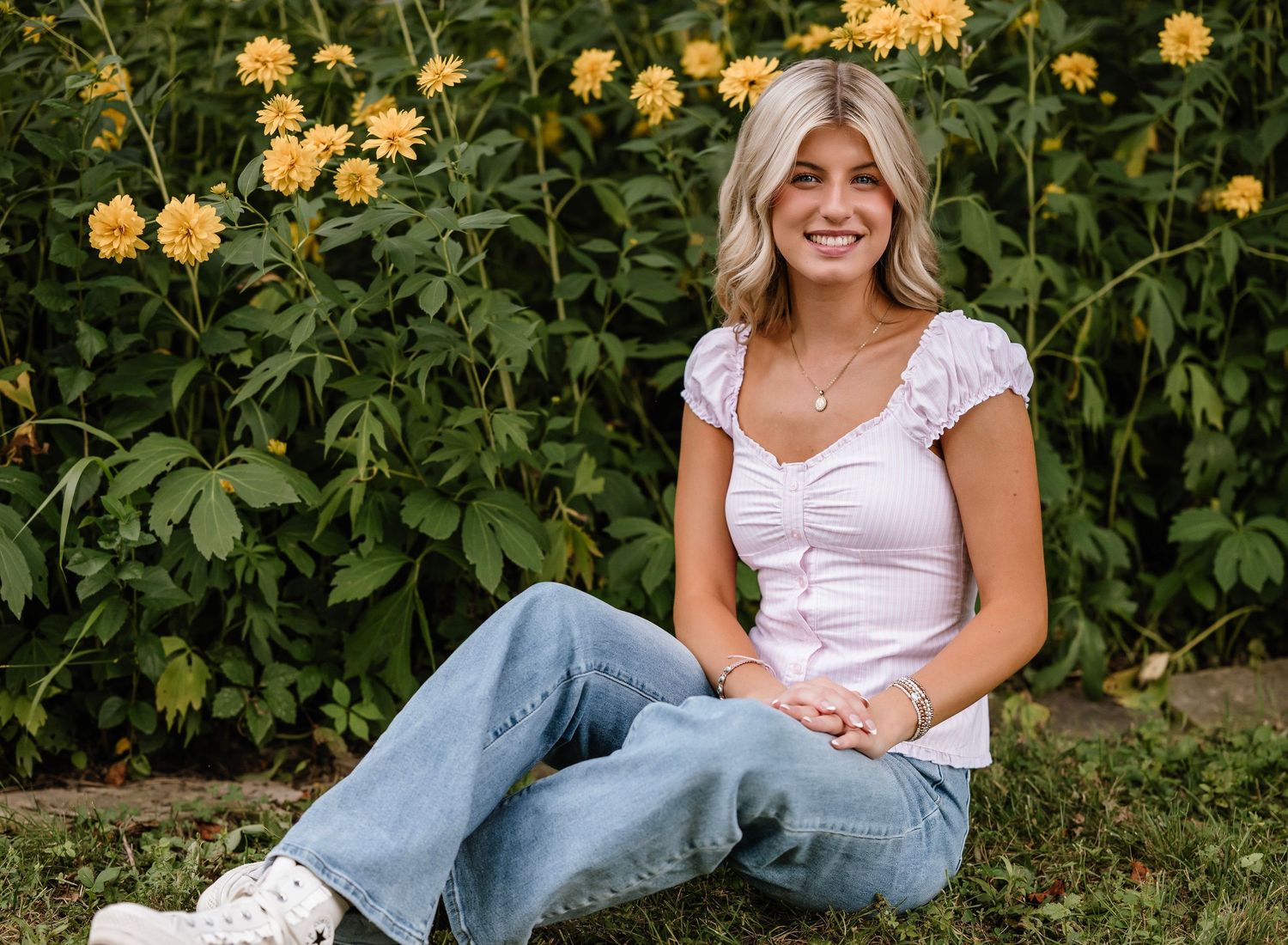 A person in jeans and a white top lounges casually in a garden with blooming yellow roses in the background.