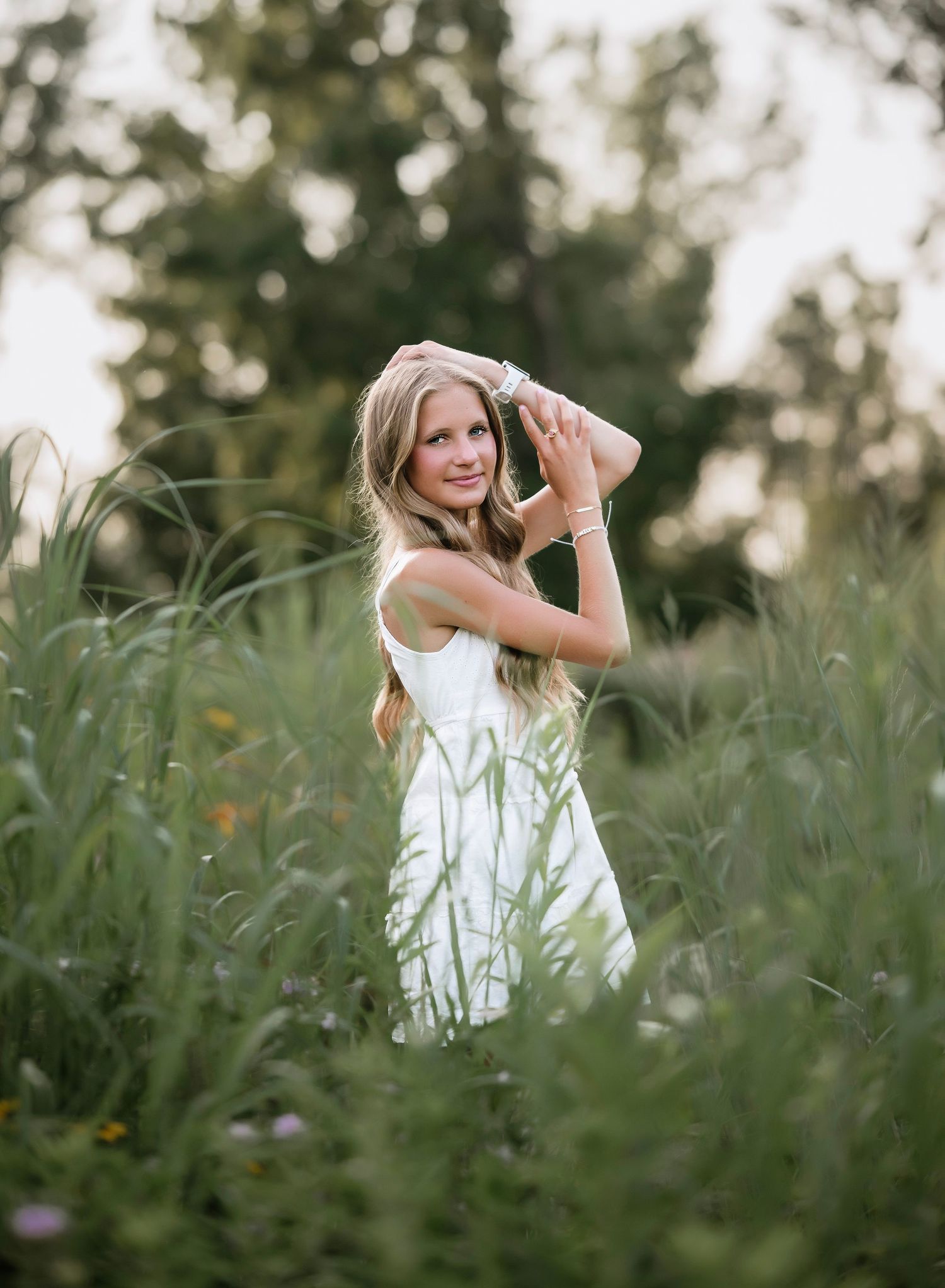 A young person in a white dress plays in a field of tall grass during golden hour lighting.