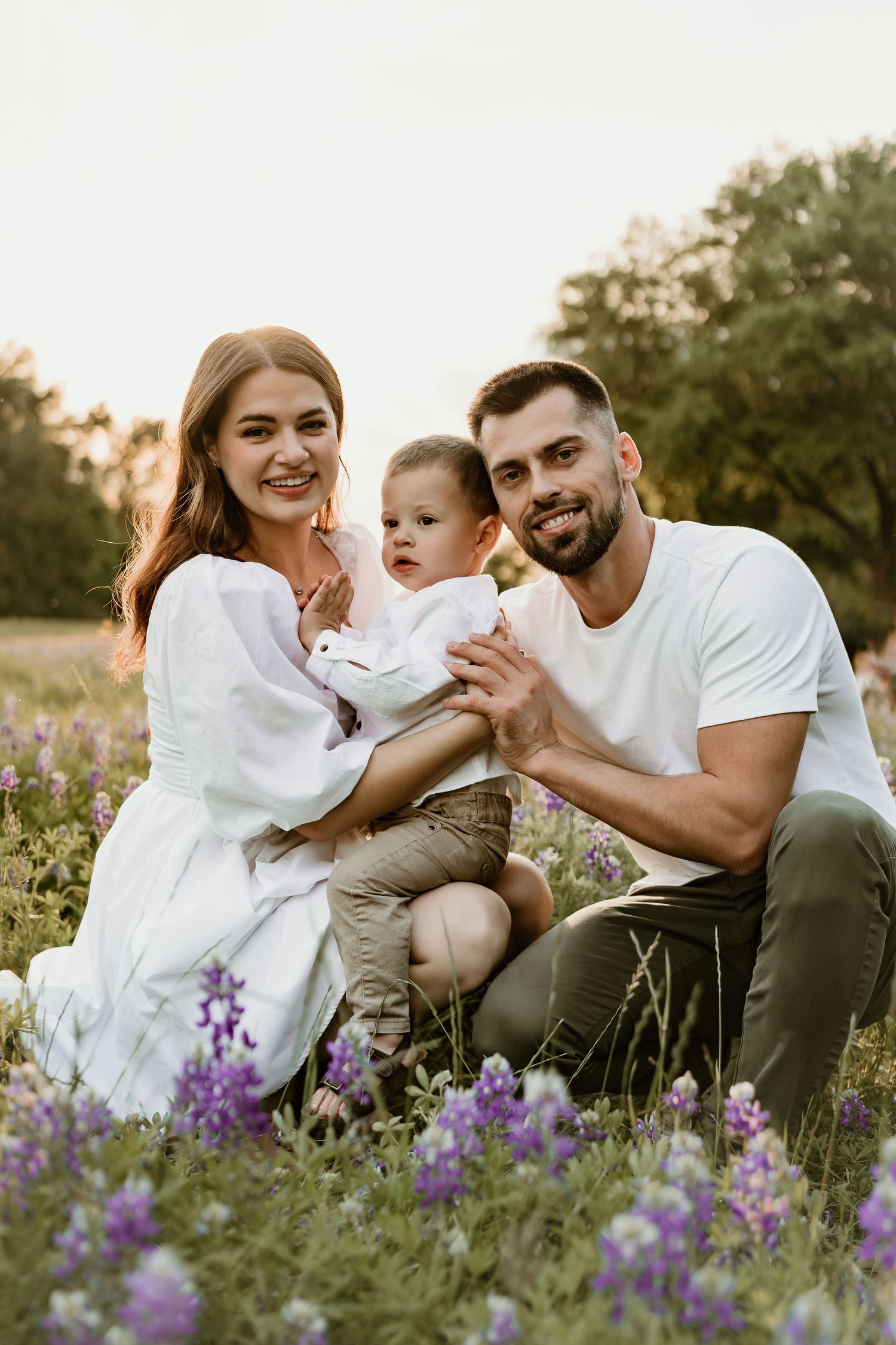 A family shares intimate moments while sitting among purple wildflowers.