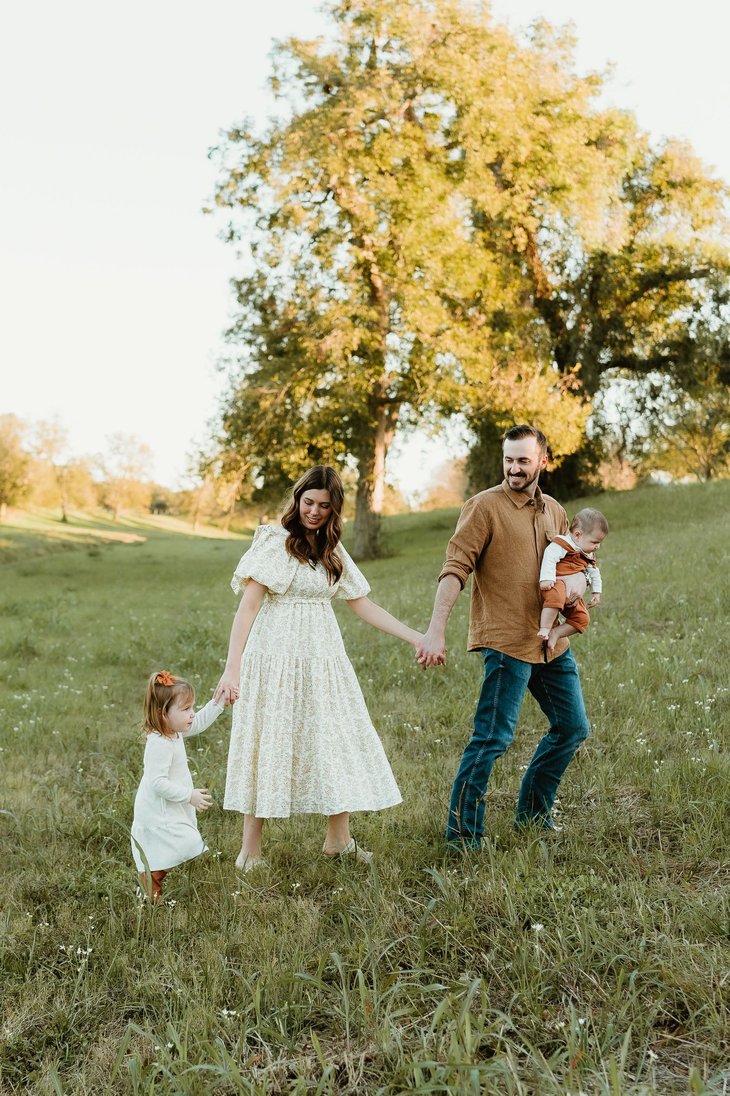 A family walks together in a grassy field during golden hour autumn light.