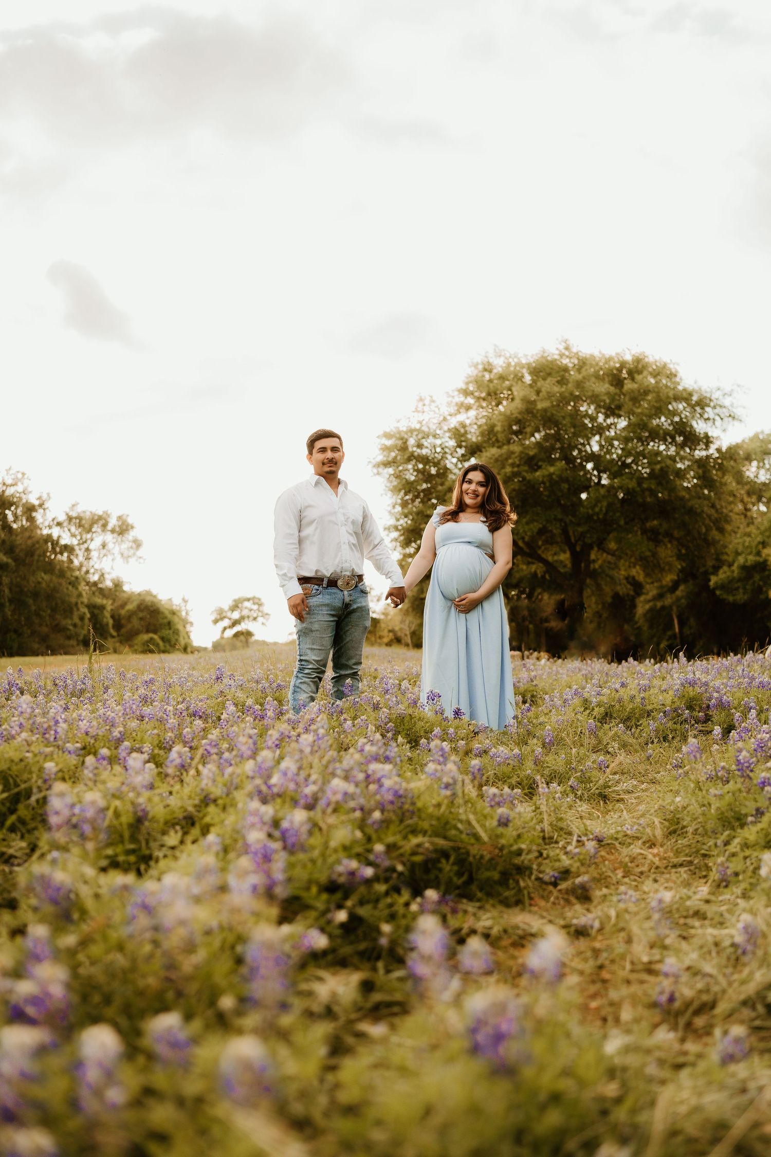 A couple poses together in a field of purple wildflowers at sunset.