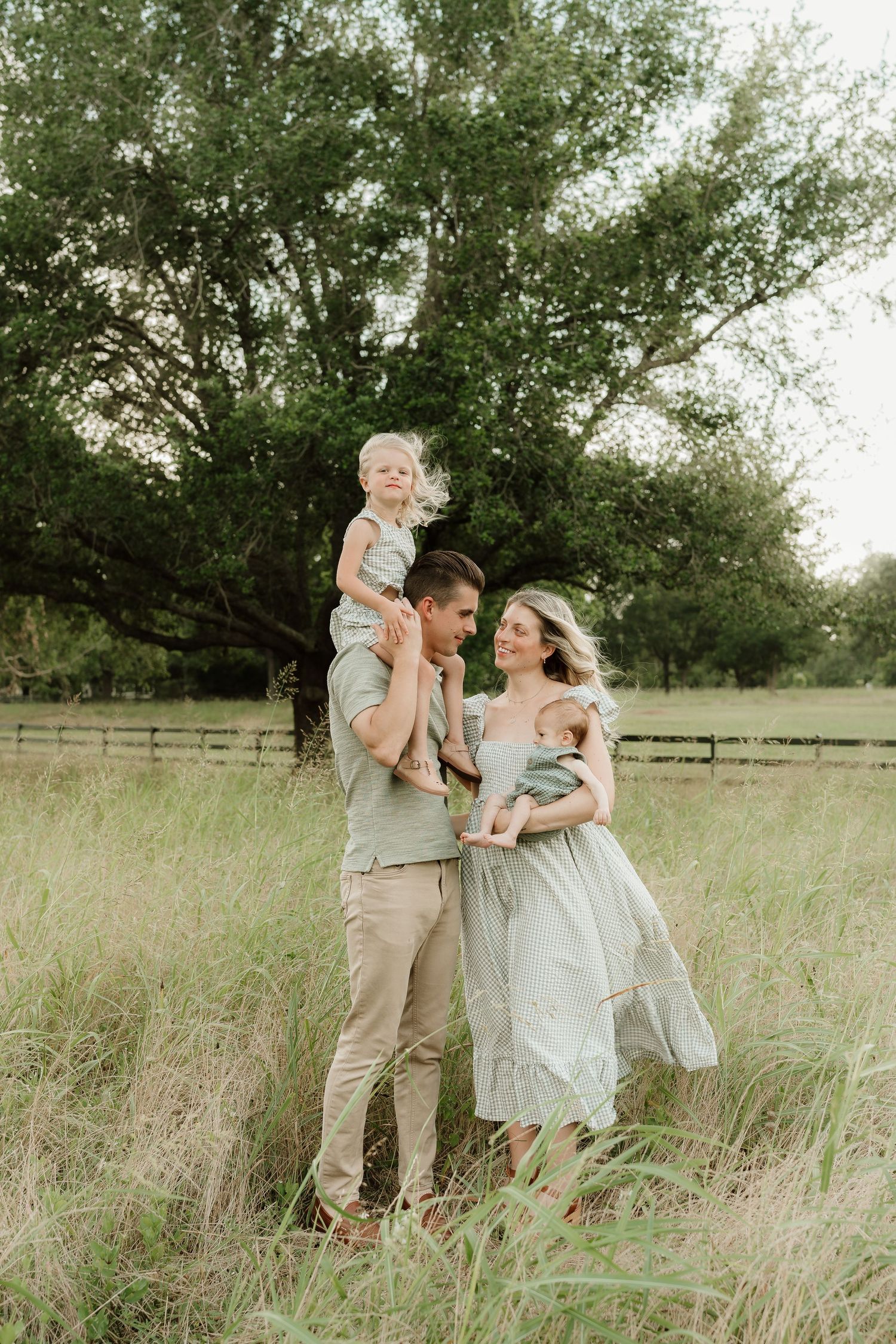 Family shares tender moments together in a sun-lit field with tall grass.