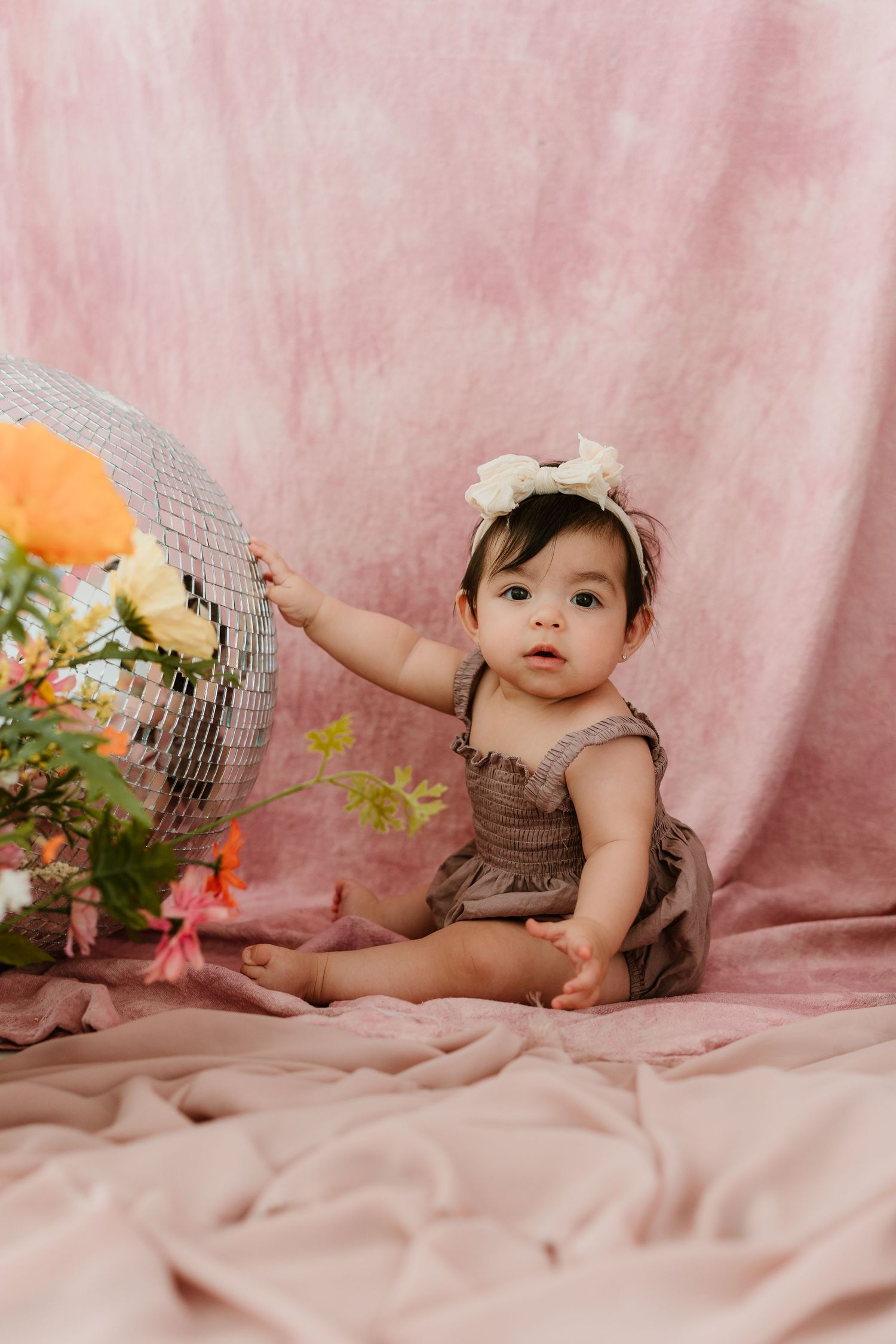 Baby in brown outfit lying on pink backdrop during milestone photo session.