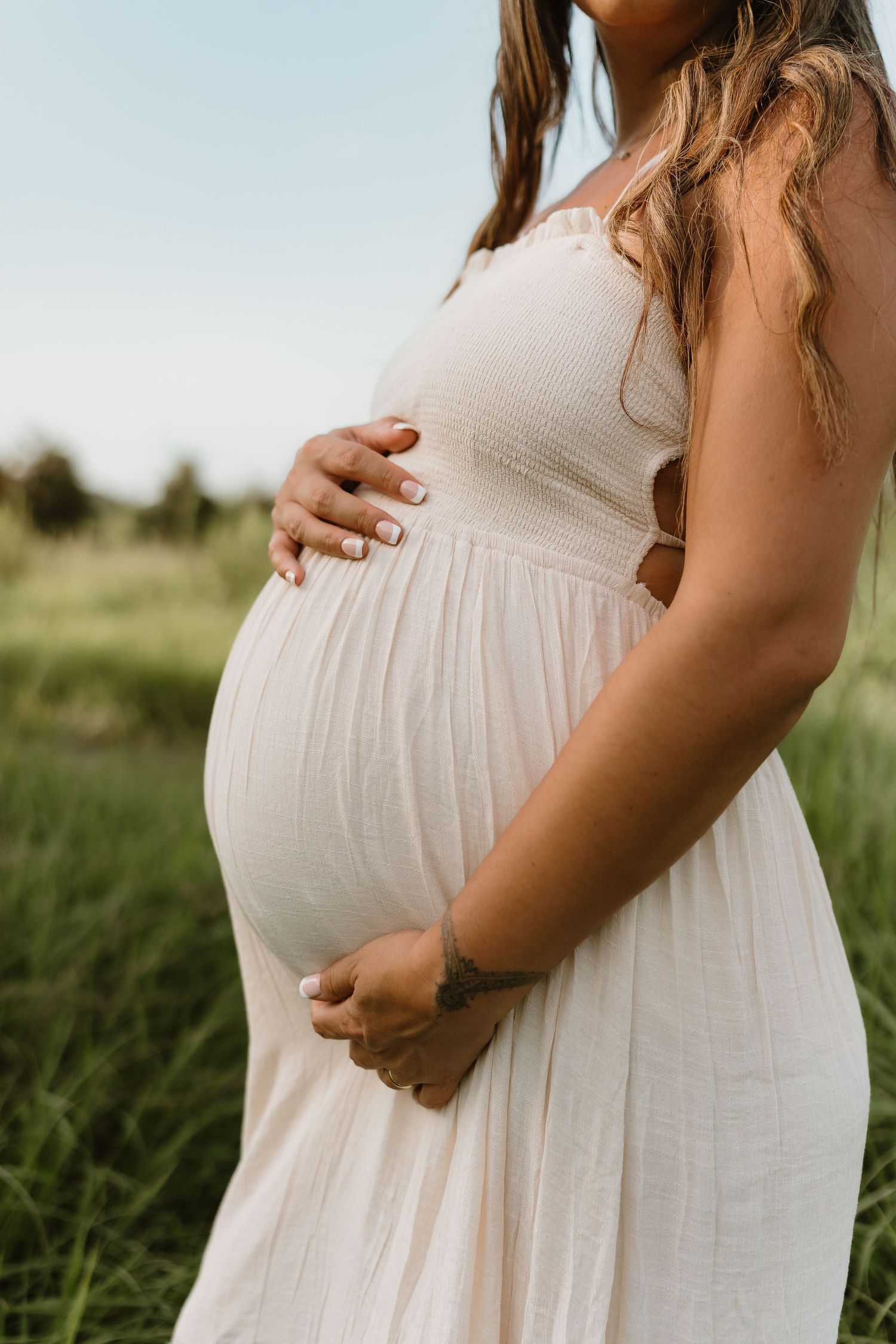 Close-up shots of a pregnant woman's belly in a white dress against natural outdoor lighting.