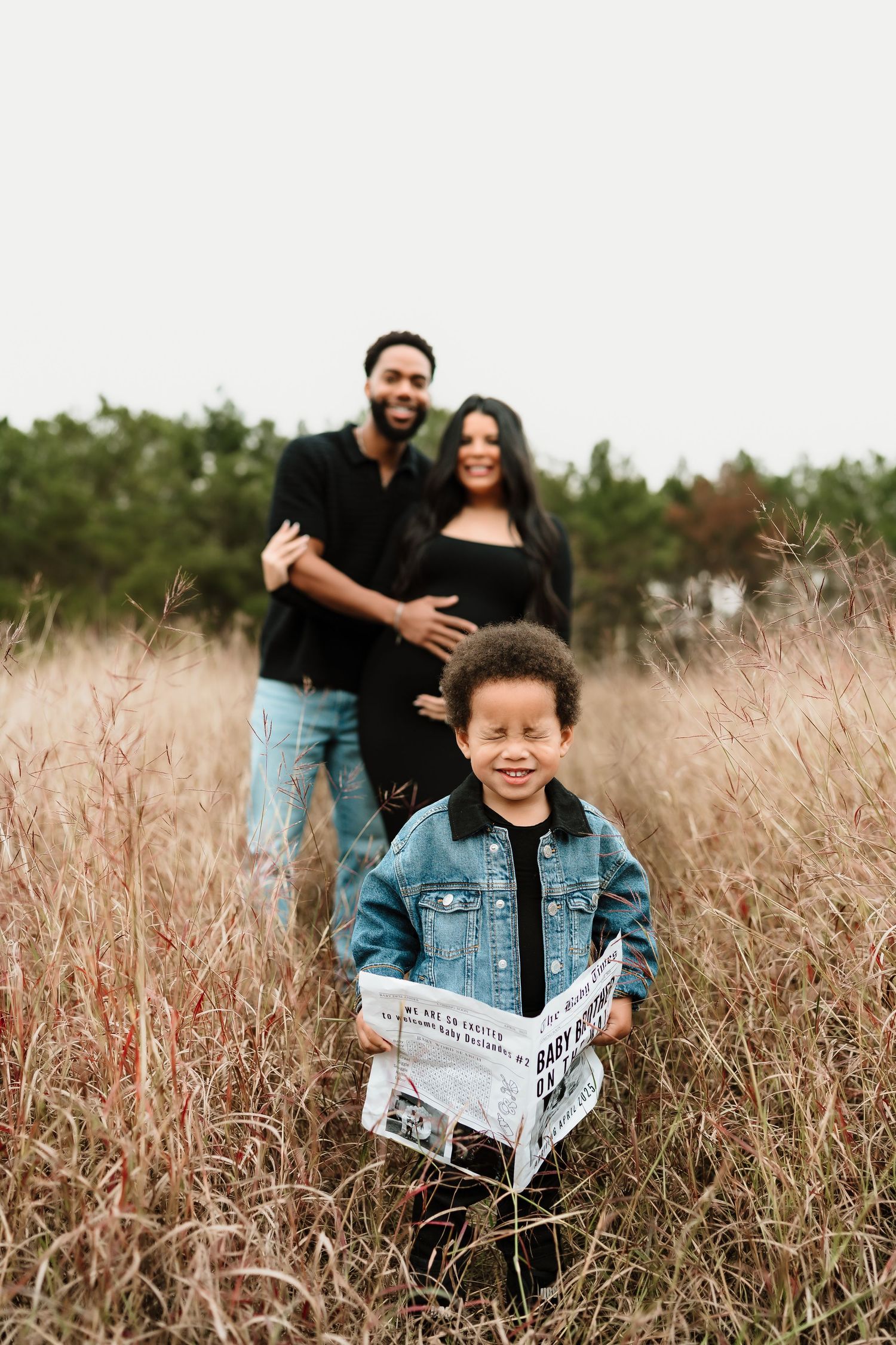 Family photoshoot in tall grass field with newspaper announcement prop.