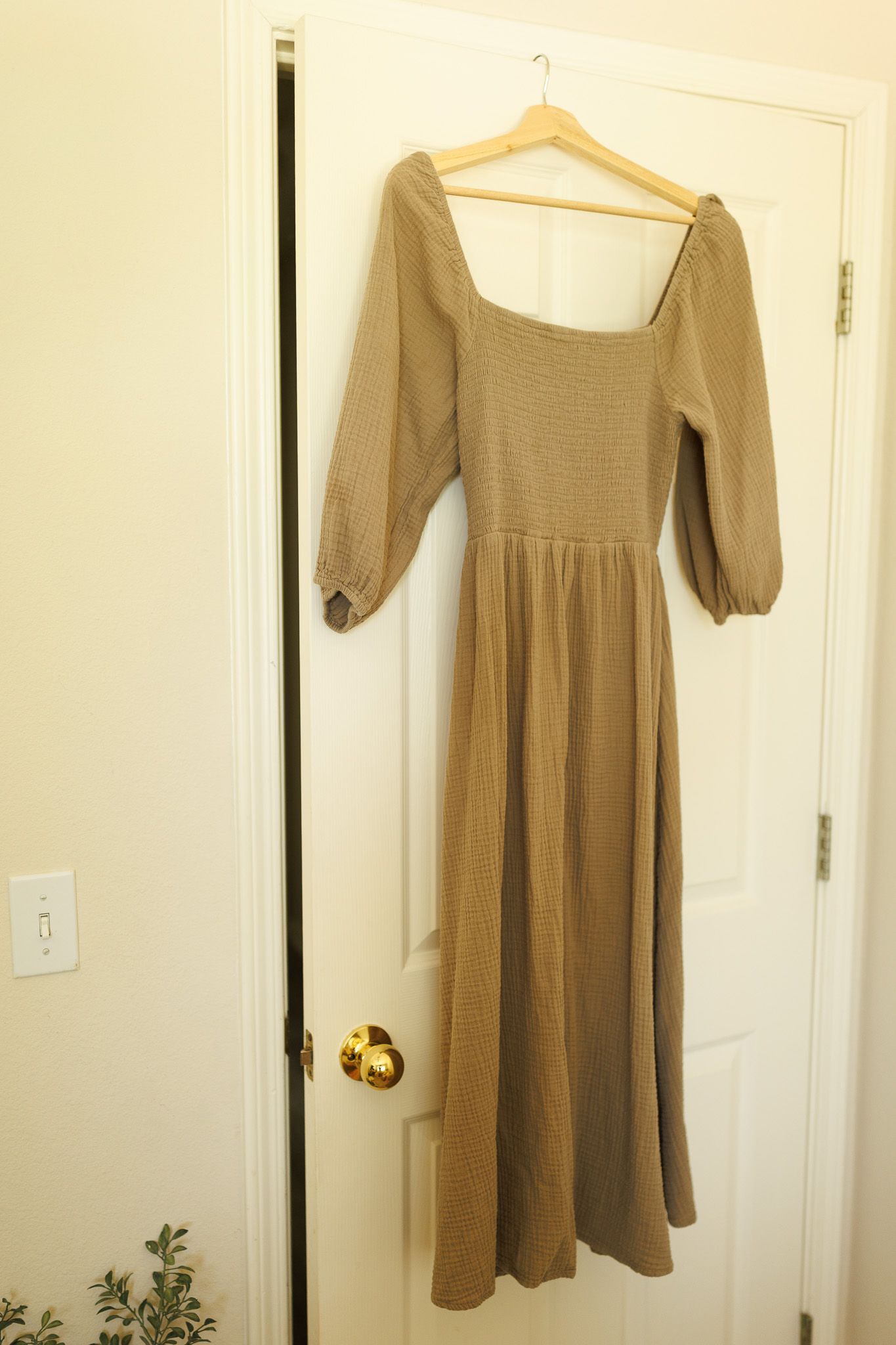 A light brown or beige babydoll dress with short puff sleeves hangs against a white door.