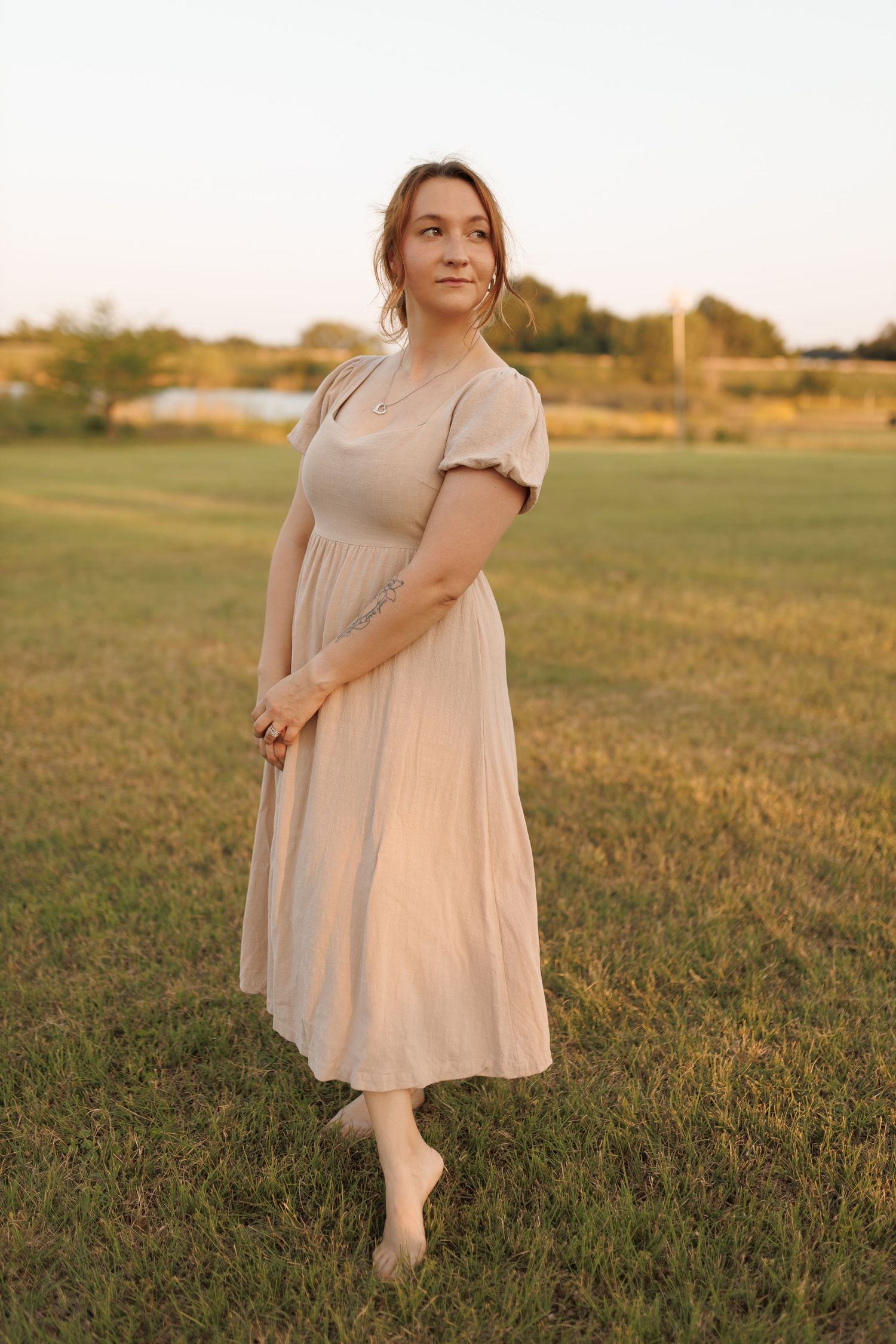 A person in a flowy beige midi dress poses gracefully in a golden field at sunset.