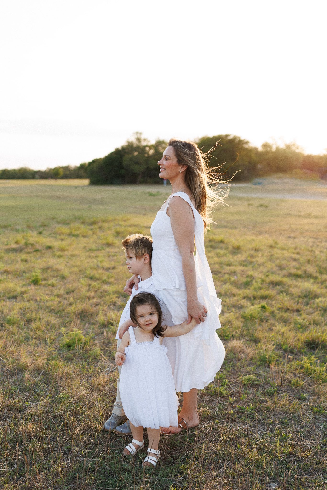 A woman in a white dress walking with two young children in a field.