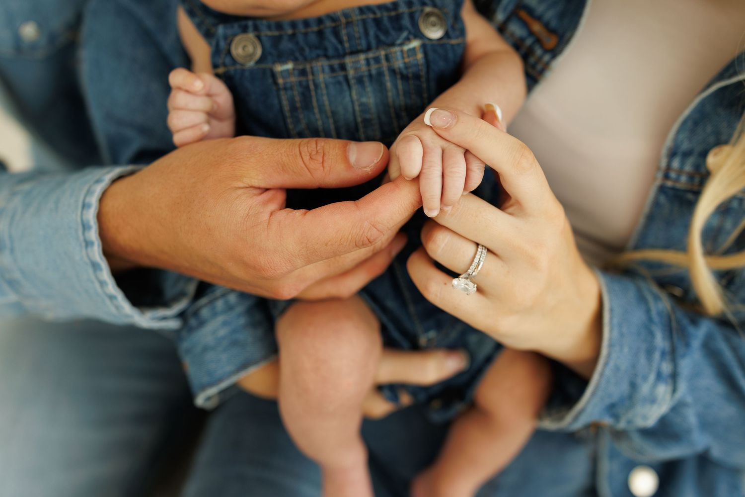 Close up of hands with a diamond engagement ring being held, wearing denim and casual clothing.
