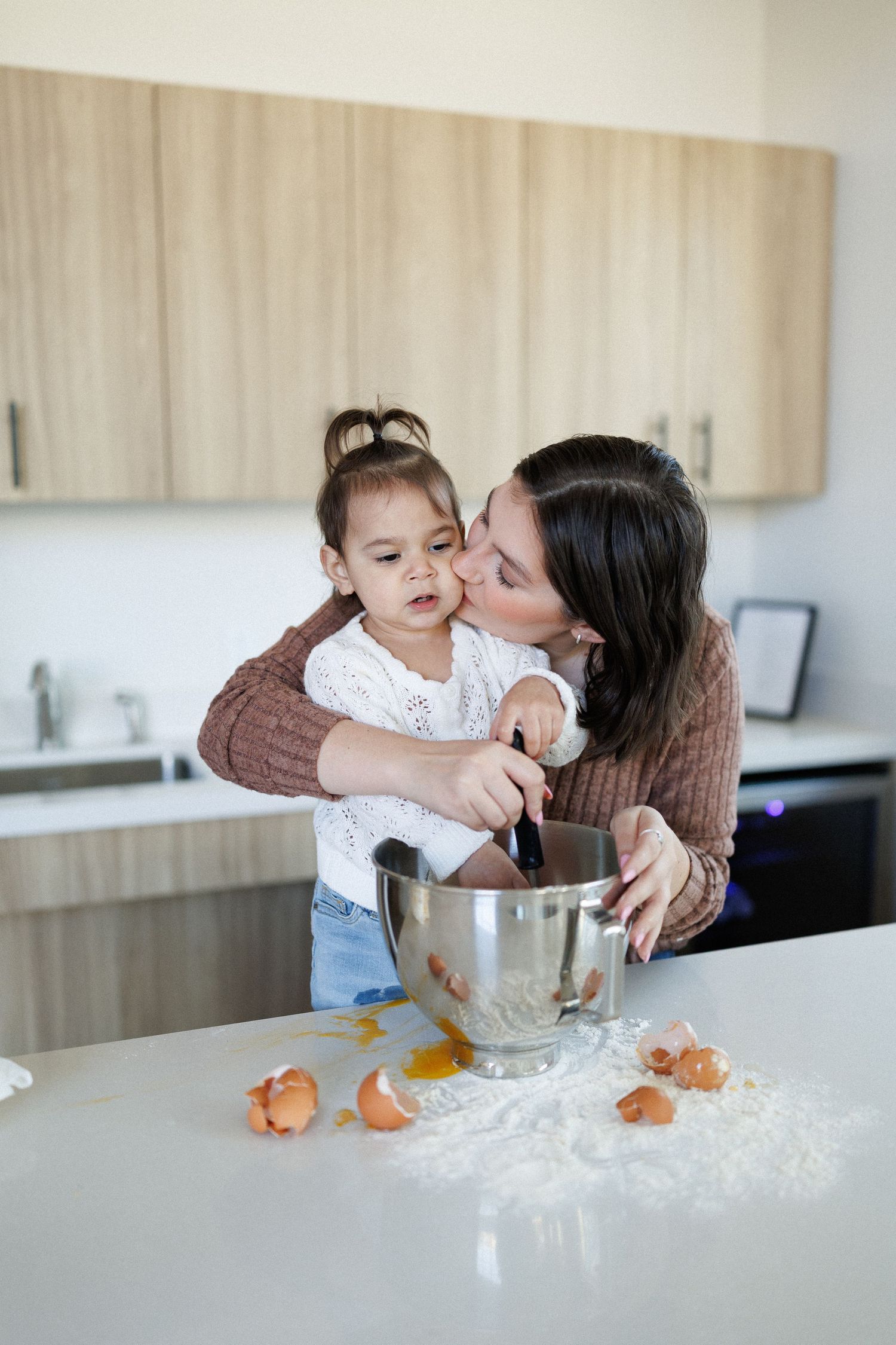 A parent and child in a modern kitchen making a mess with flour while baking together.