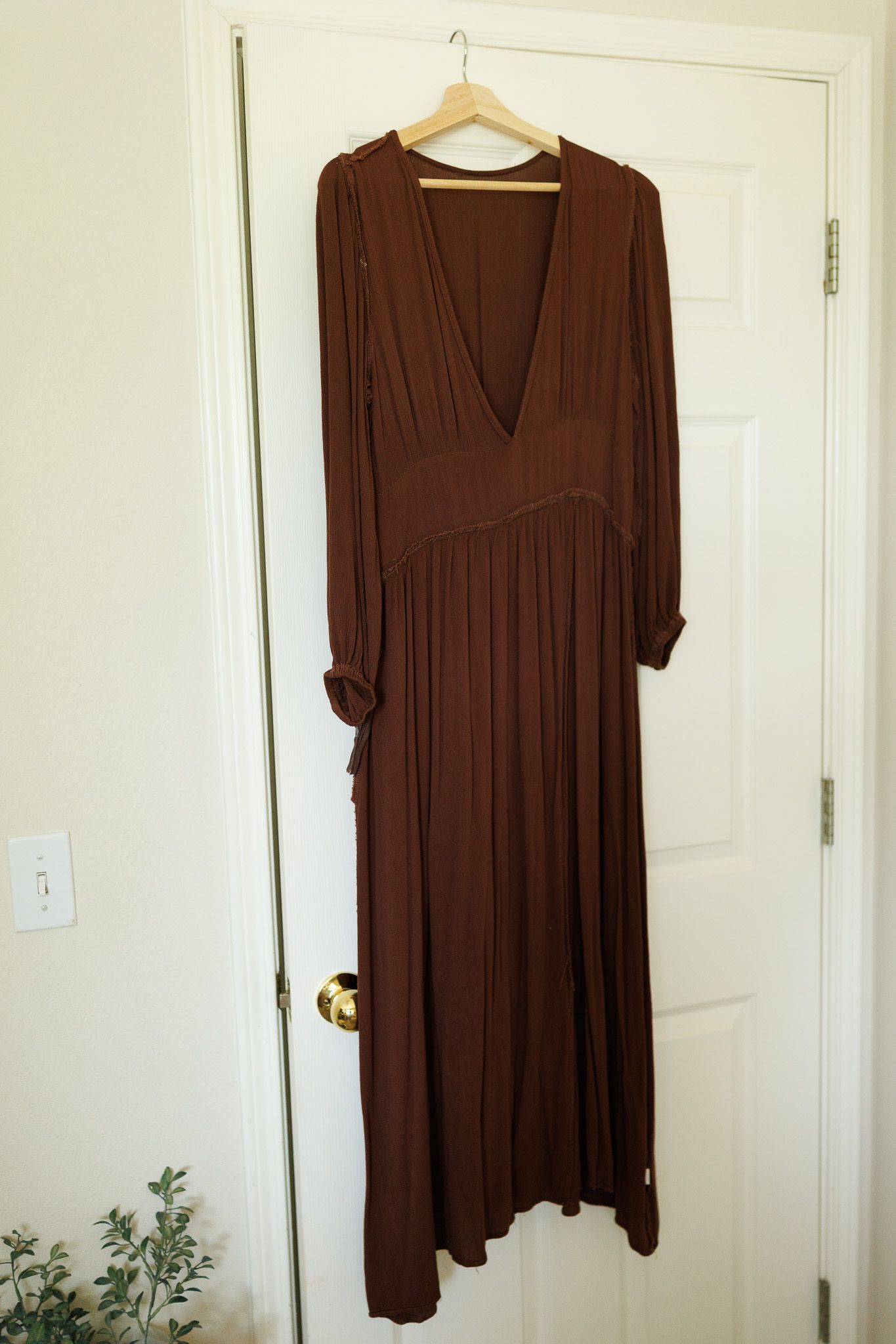 Long-sleeved brown knit dress hanging on white wooden hanger against white door.