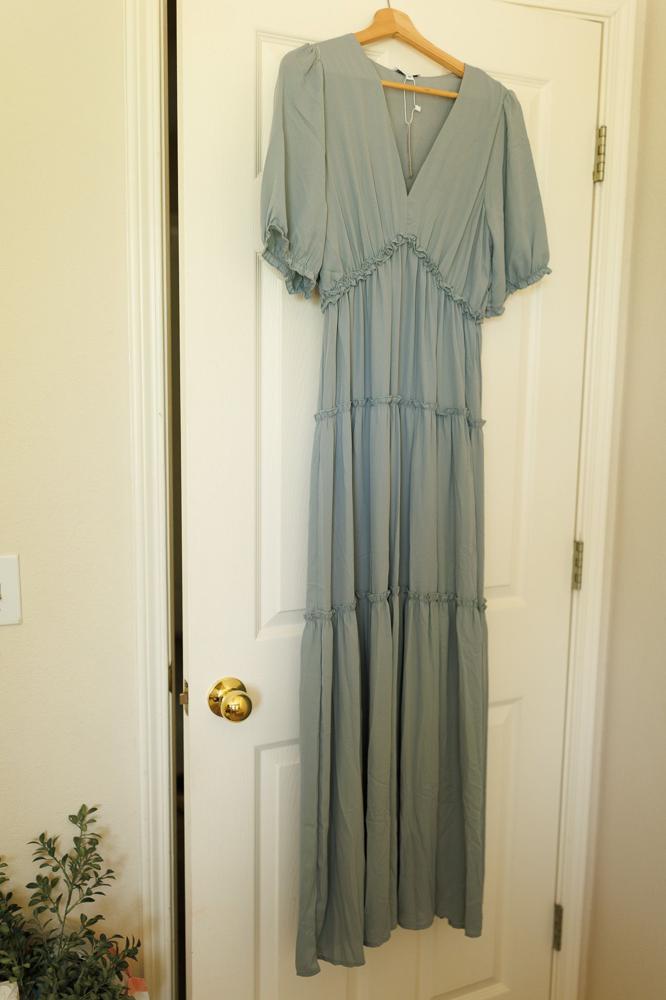 Light sage green tiered babydoll dress with short sleeves hanging on white wooden door against cream wall.