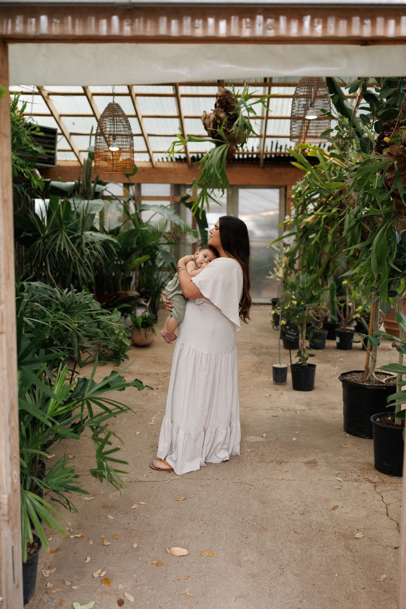 A greenhouse interior filled with potted plants and greenery along with a person in white dress seated among them.