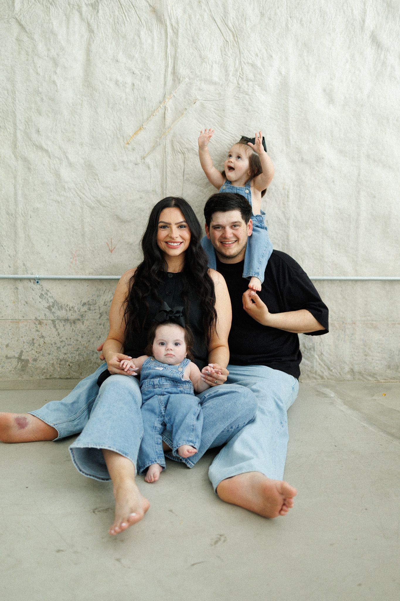 A family of three, including a woman, man, and child, sitting together on the floor and smiling.