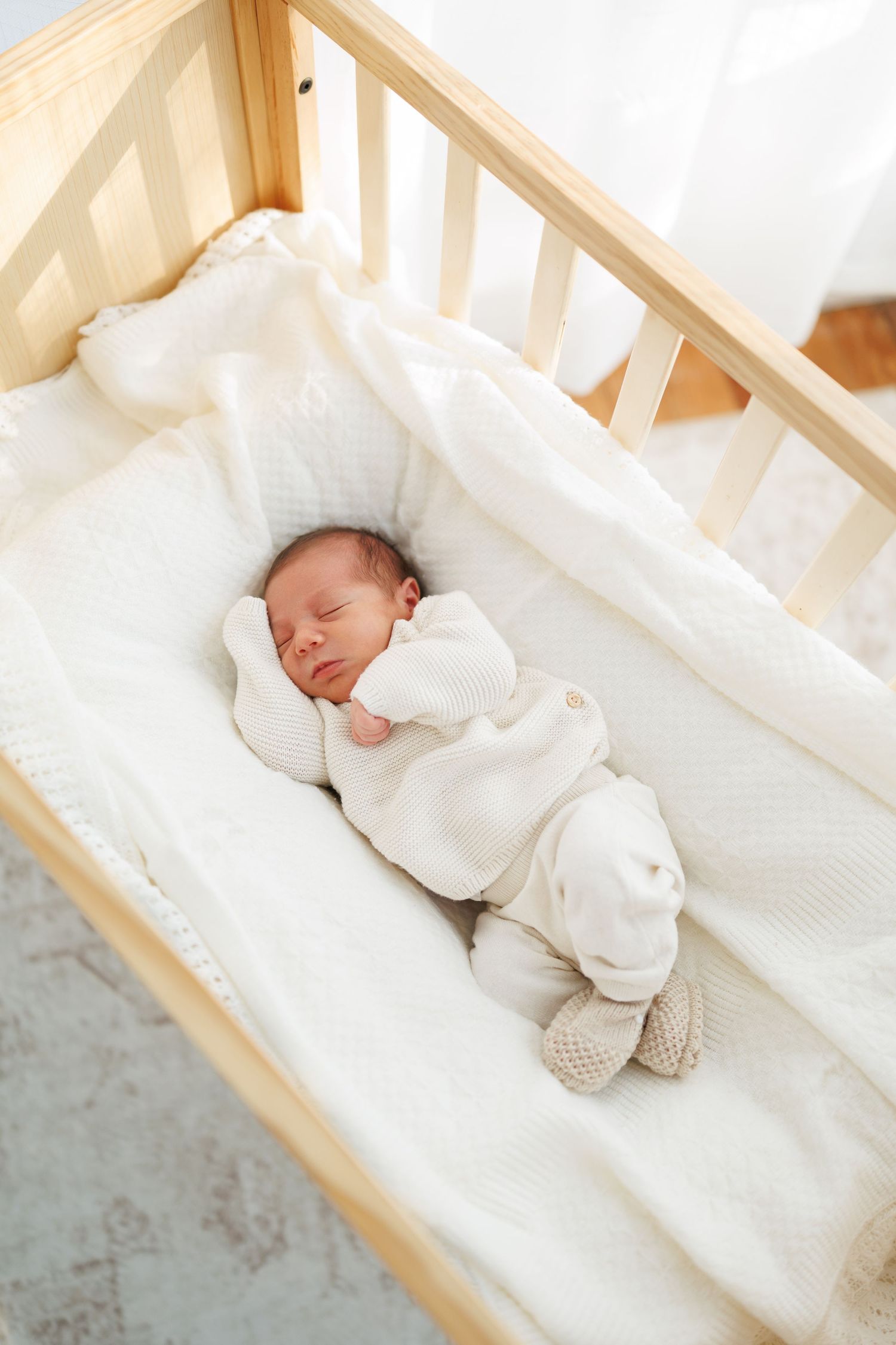 Sleeping baby in cozy white crib wearing soft knit outfit against neutral bedding.