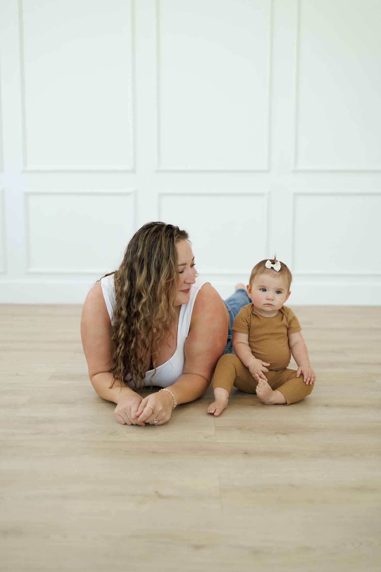 Baby and adult laying on hardwood floor in minimalist white room for creative milestone photo session.