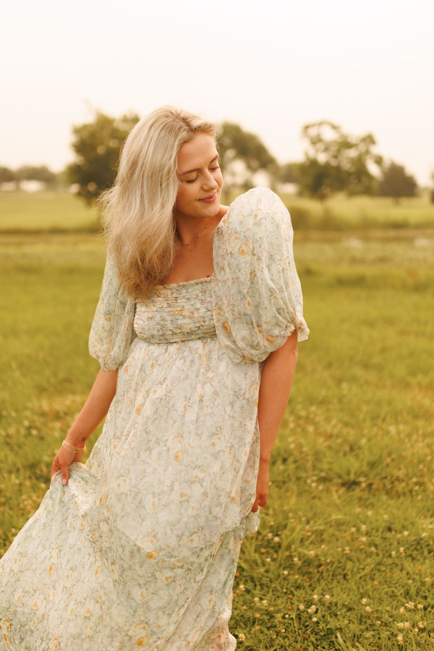 Romantic vintage-style floral dress with puffy sleeves photographed in a grassy field during golden hour.