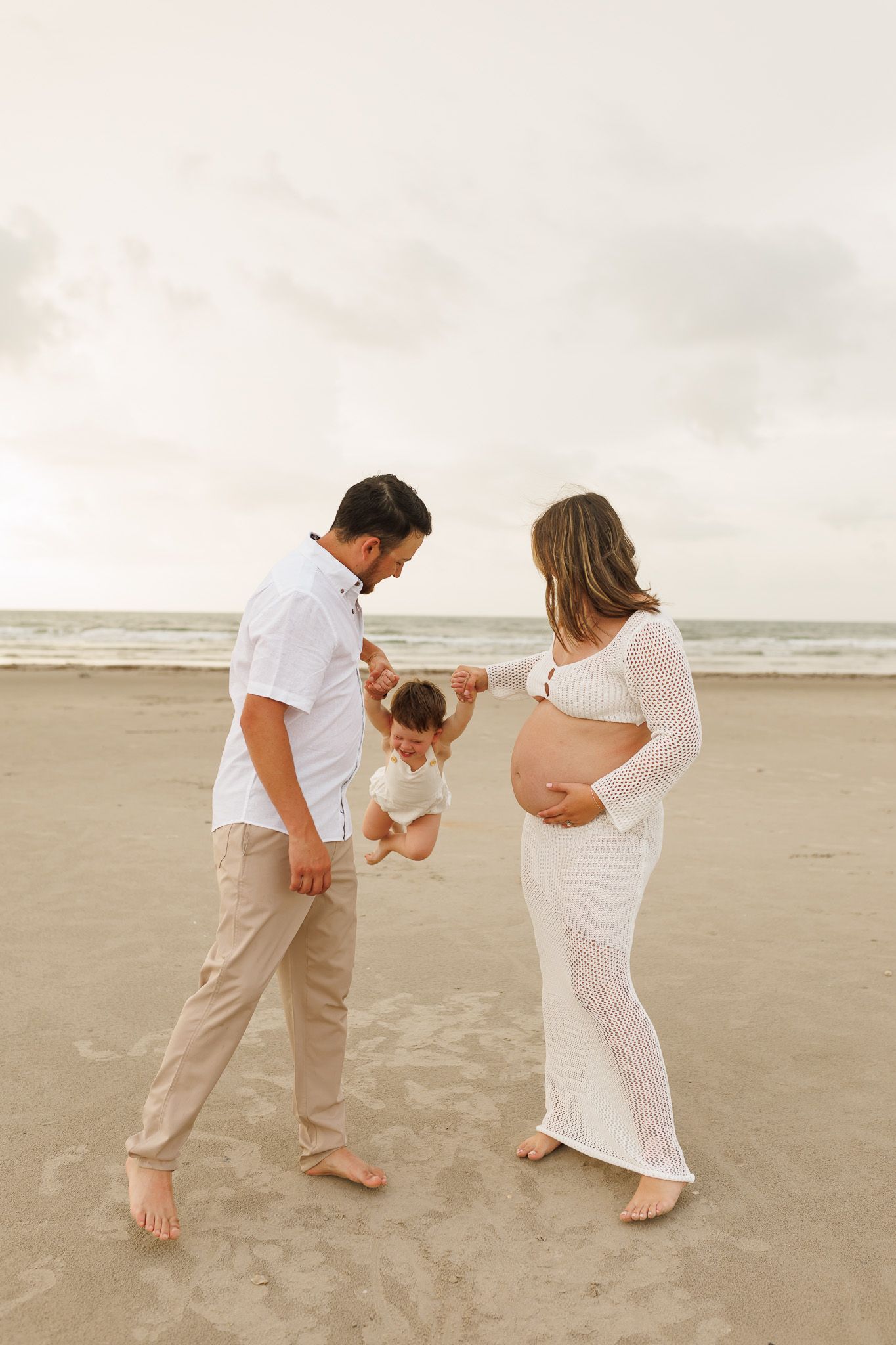 A couple and toddler play together on a beach during maternity photoshoot at sunset.