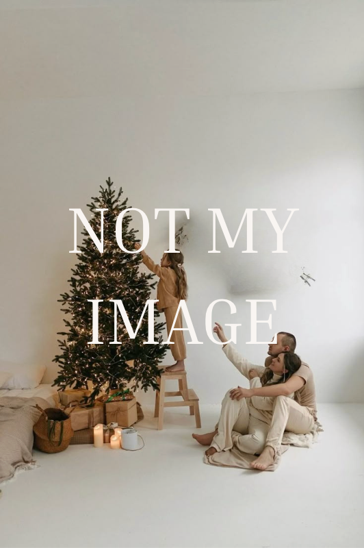 Family decorating a Christmas tree together in a bright white room with candles and gifts on the floor.
