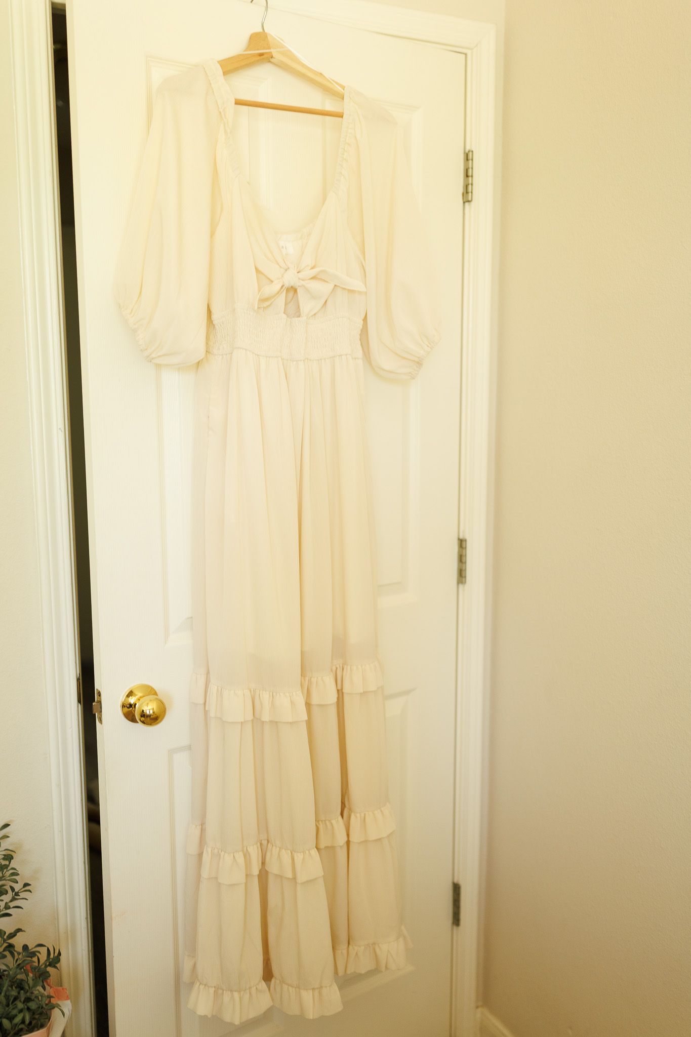 Vintage white nightgowns and dresses hanging on hangers against a cream-colored wall.