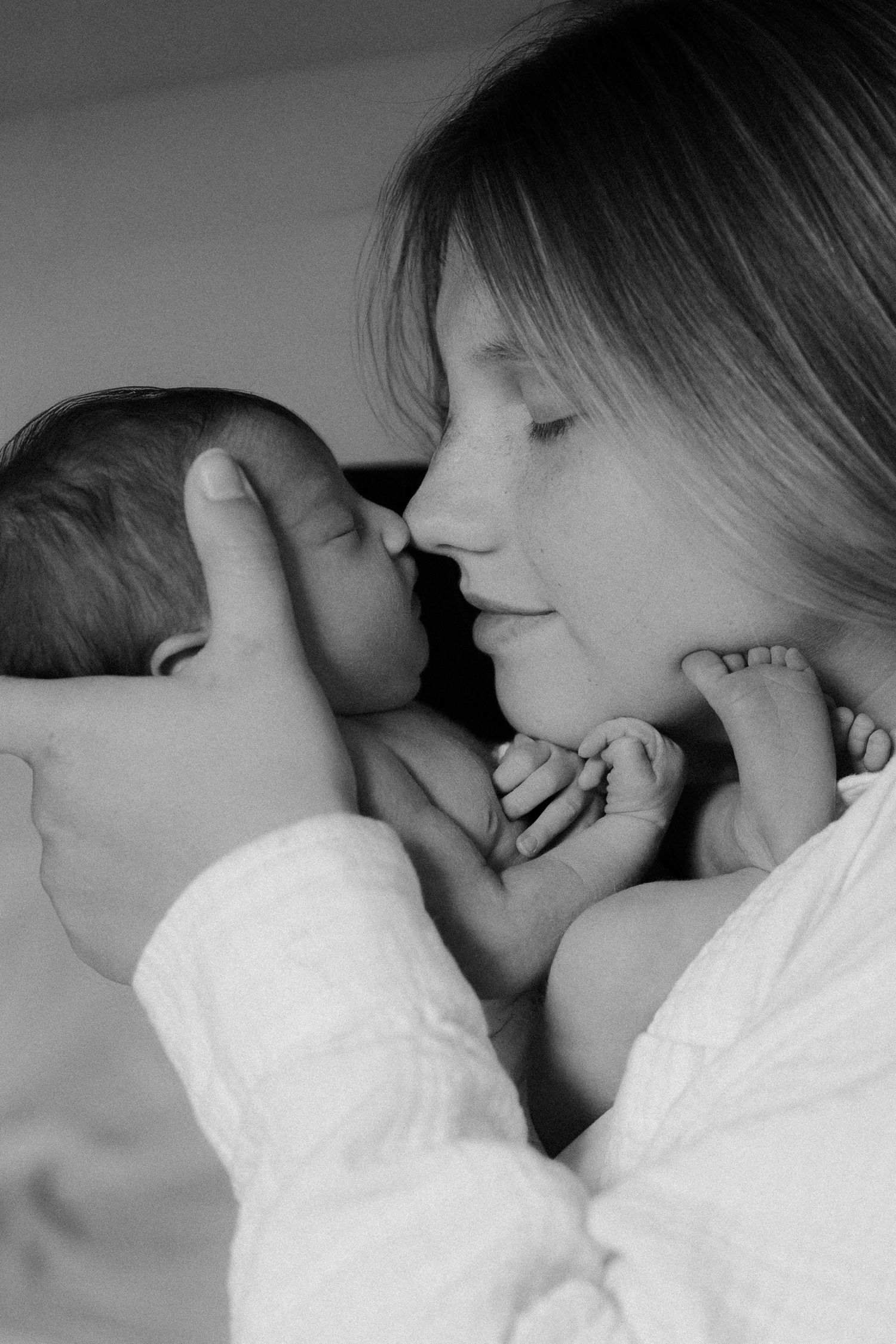 Black and white photo of a mother tenderly holding her newborn baby close to her face.