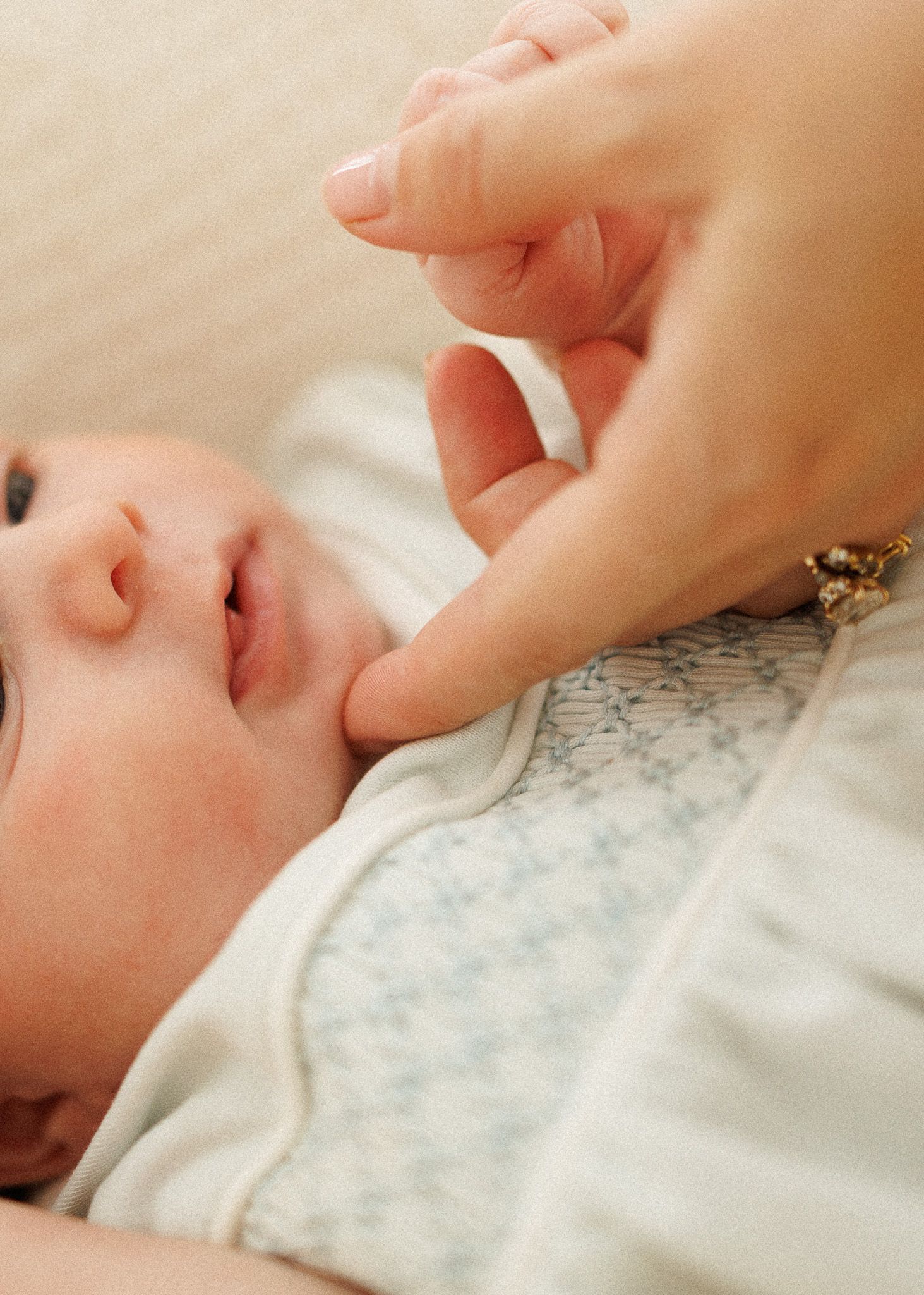 A newborn baby lying down while an adult gently touches their cheek, wearing a white onesie.