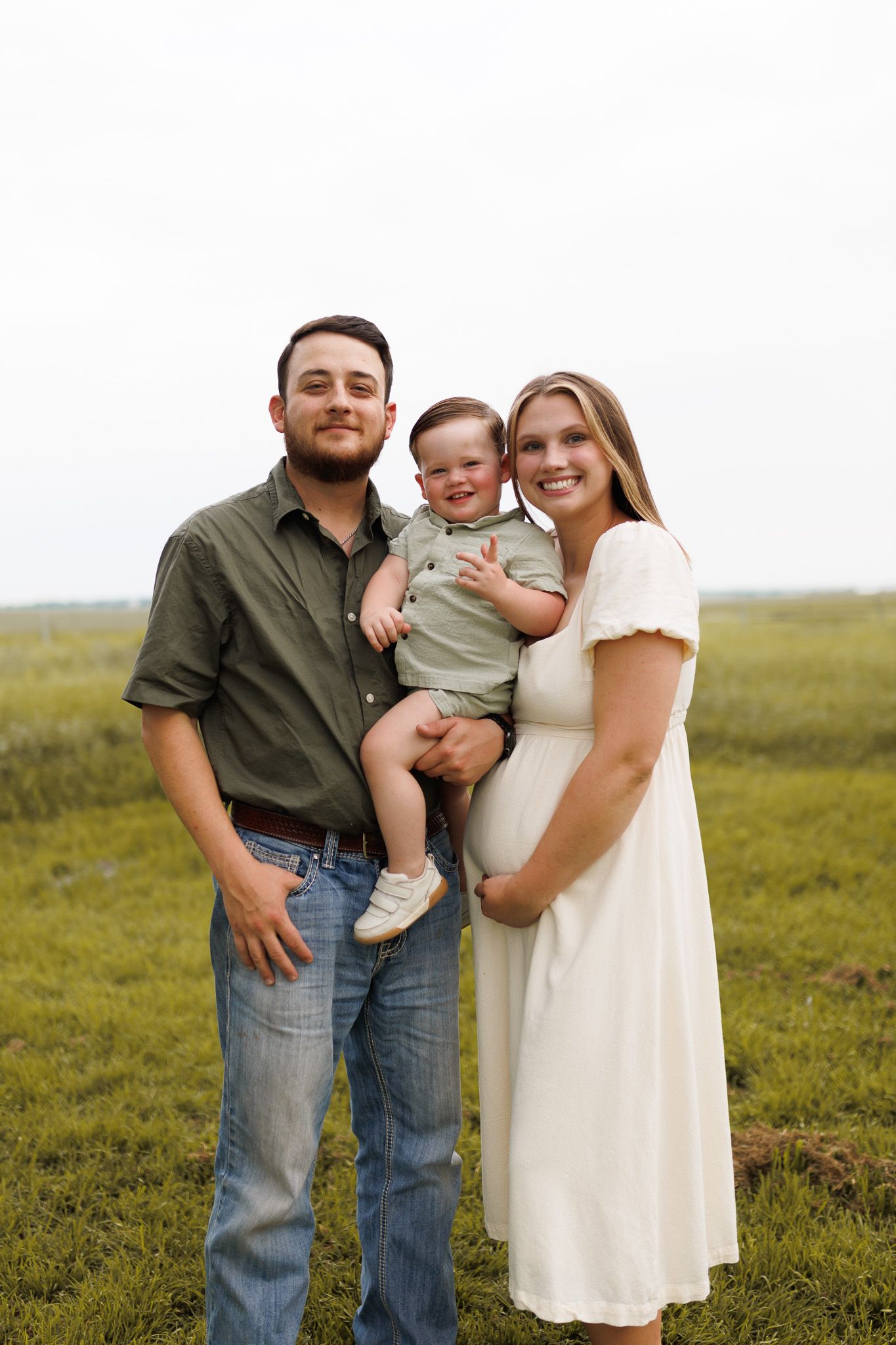 A family poses together on a grassy field during a casual outdoor photo session.