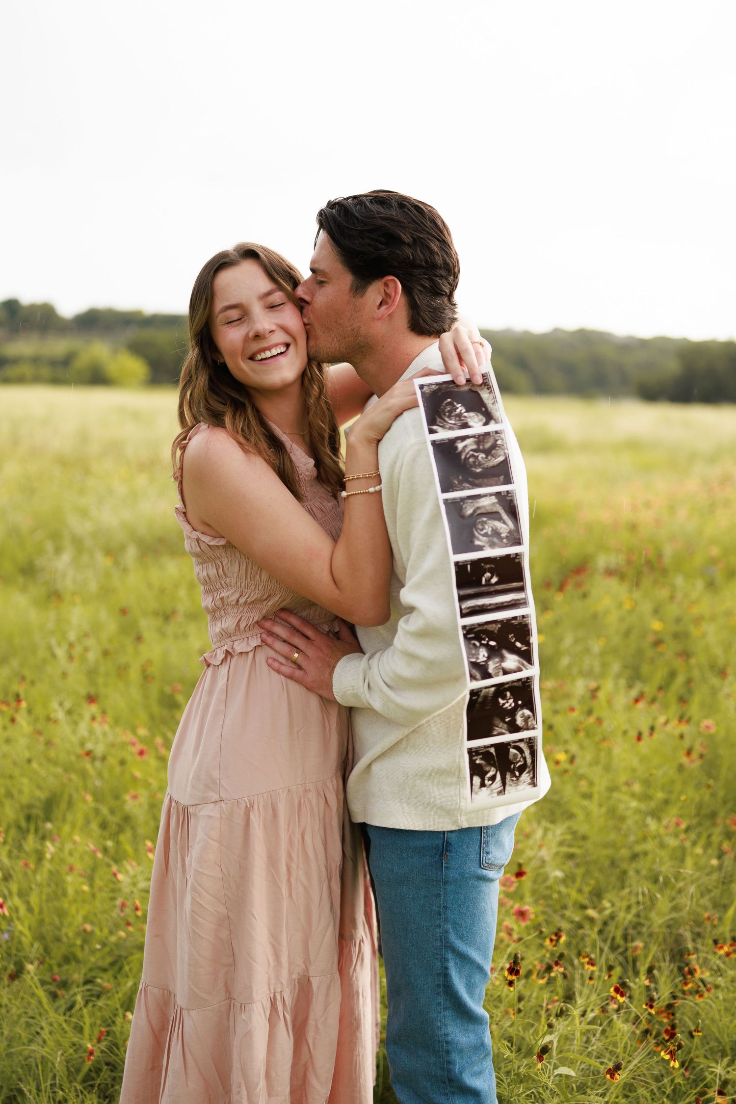 Happy couple embracing in a flower field, holding ultrasound photos, announcing their pregnancy outdoors.