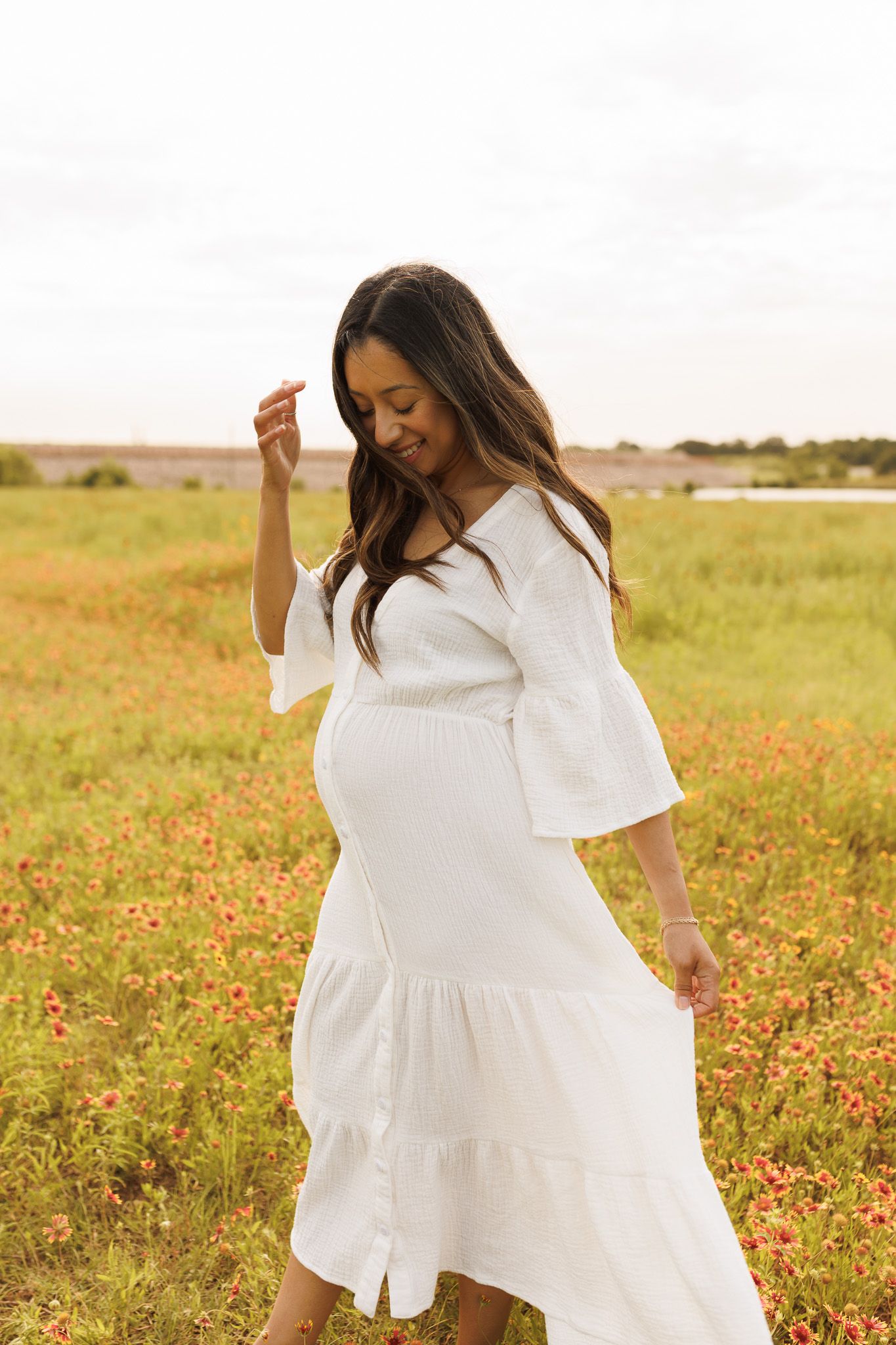 Dancing with joy in a white dress through a colorful wildflower field during golden hour.