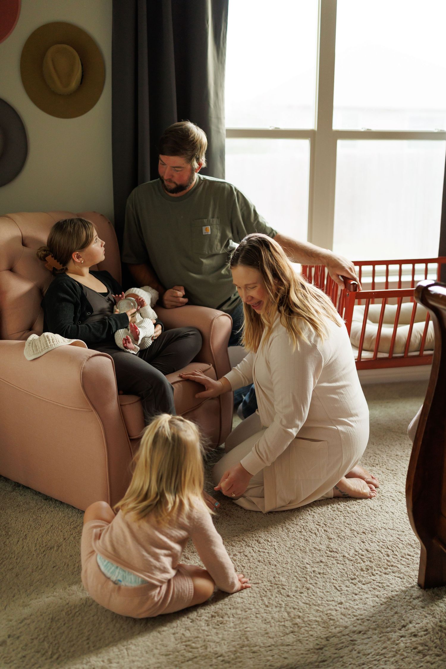 A family sits together on a beige couch in a cozy living room with natural lighting streaming through windows.