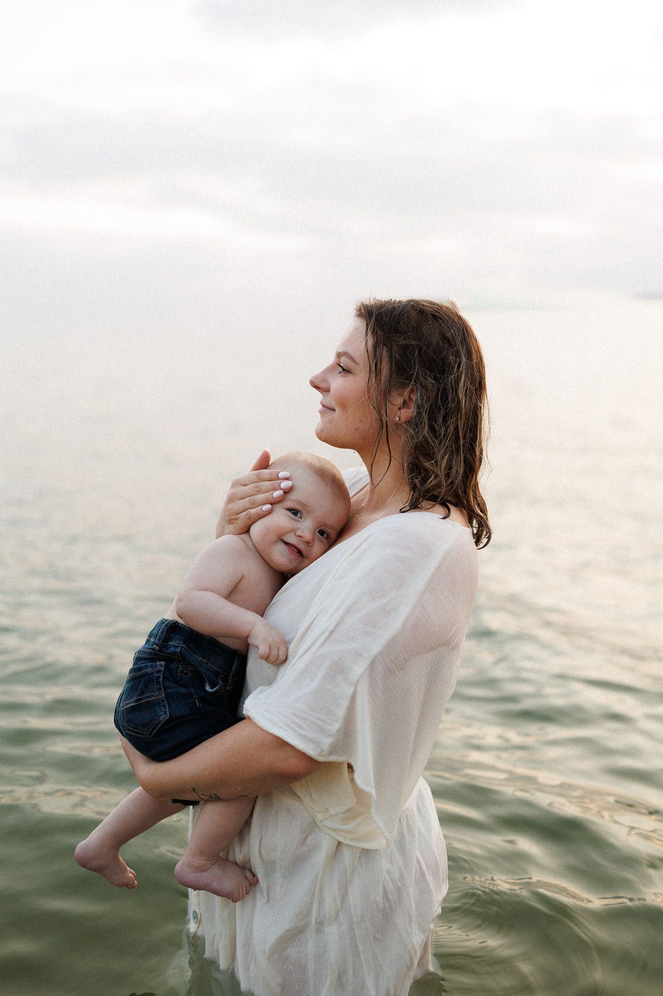 A woman holding a baby in her arms while standing in the water.