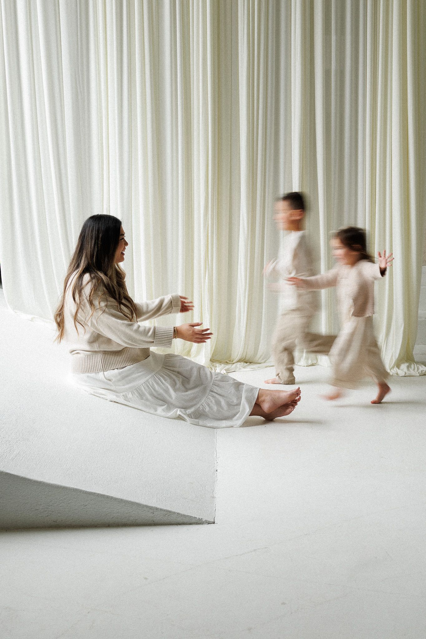Artistic sequence showing figures in white clothing moving across a minimalist white room with flowing curtains.