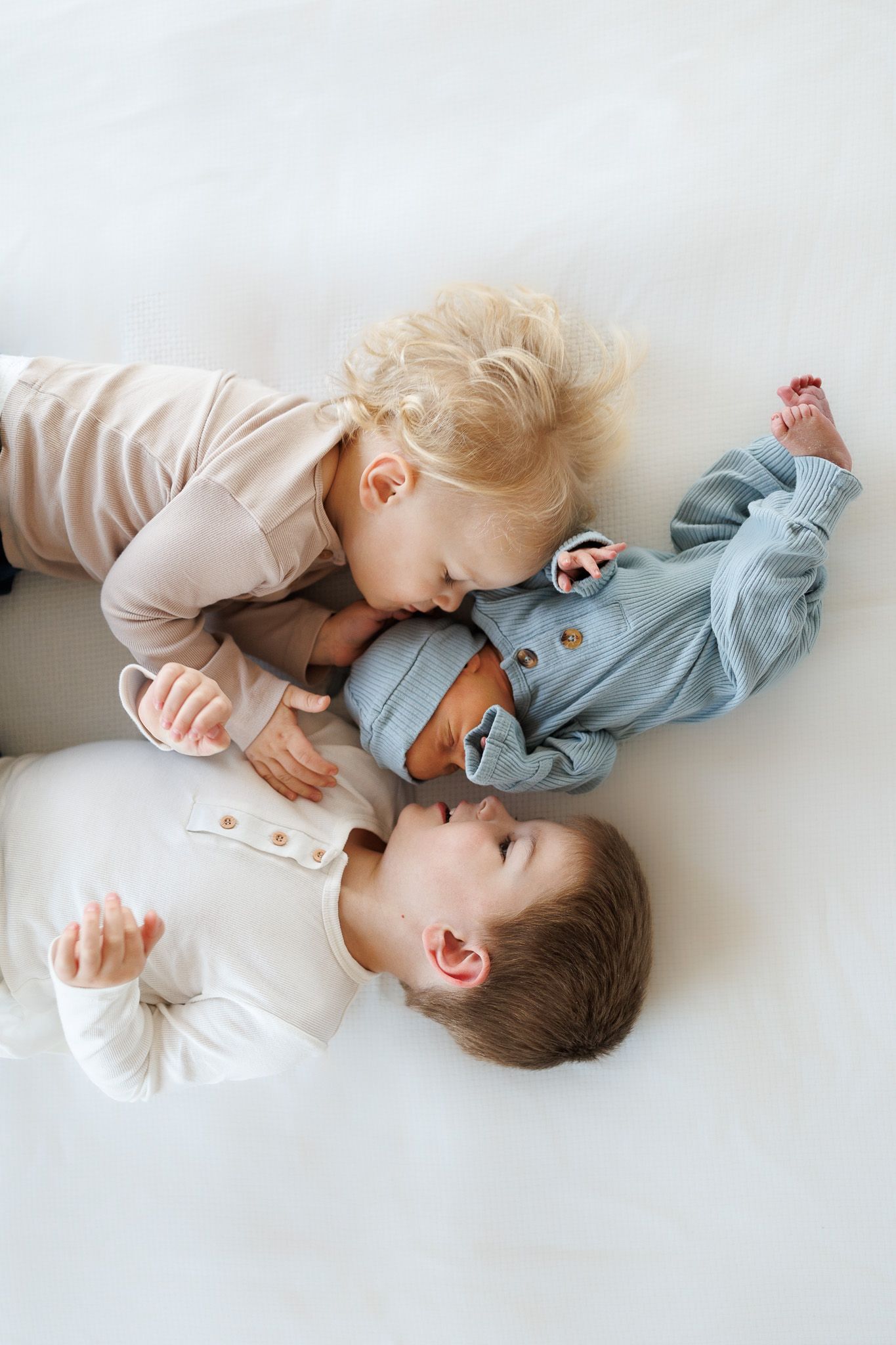 Two young children in soft colored outfits lying together on white background showing sweet sibling affection.